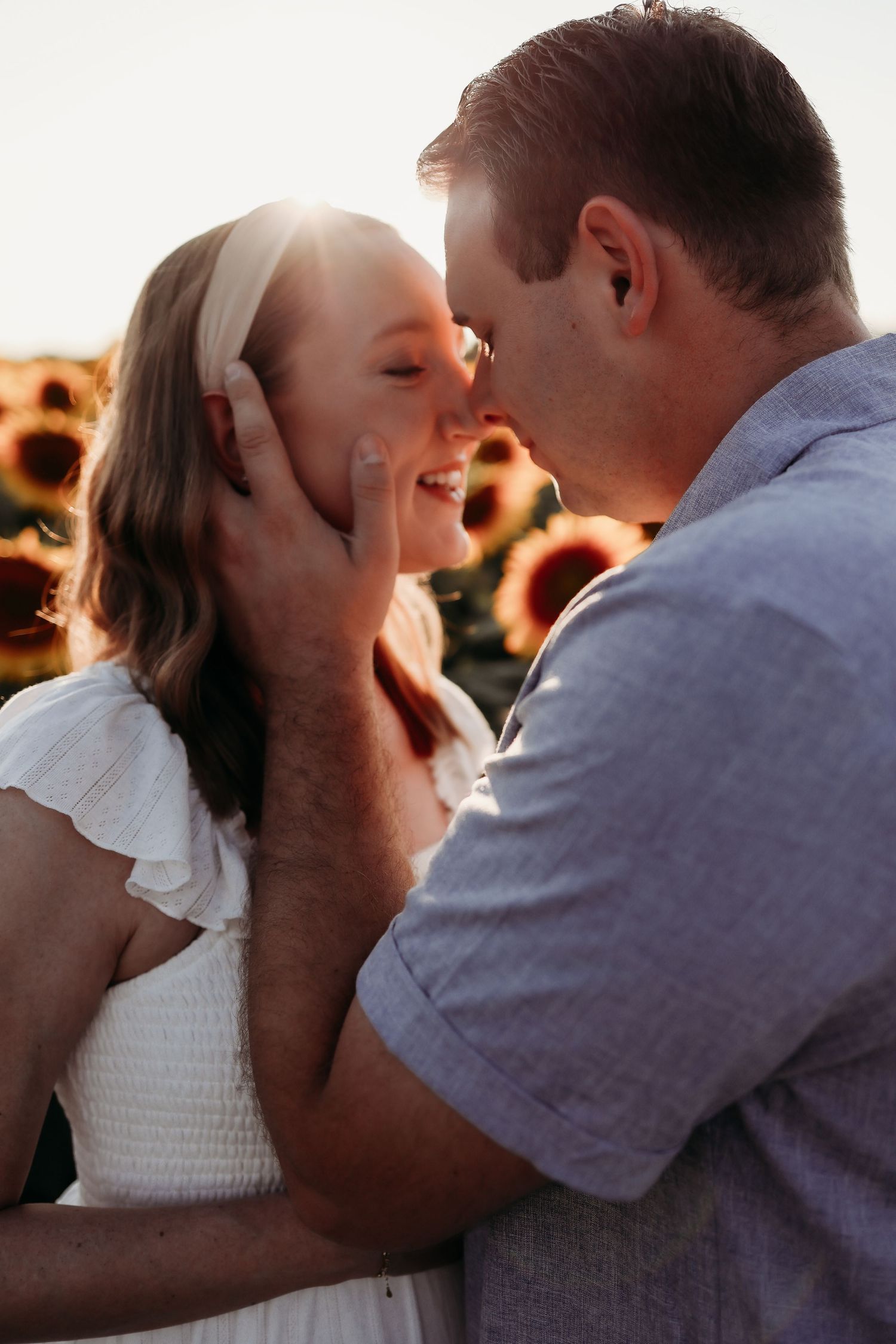 Couple sharing a romantic moment in a sunflower field at golden hour, man tenderly holding woman's face.