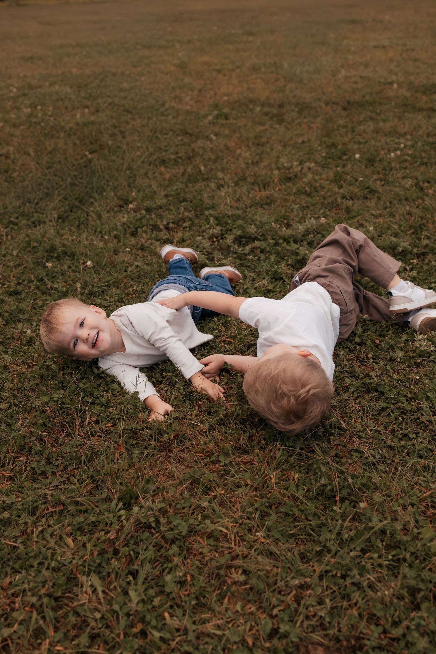 Two happy toddlers in white shirts playing and laughing together on green grass outdoors.