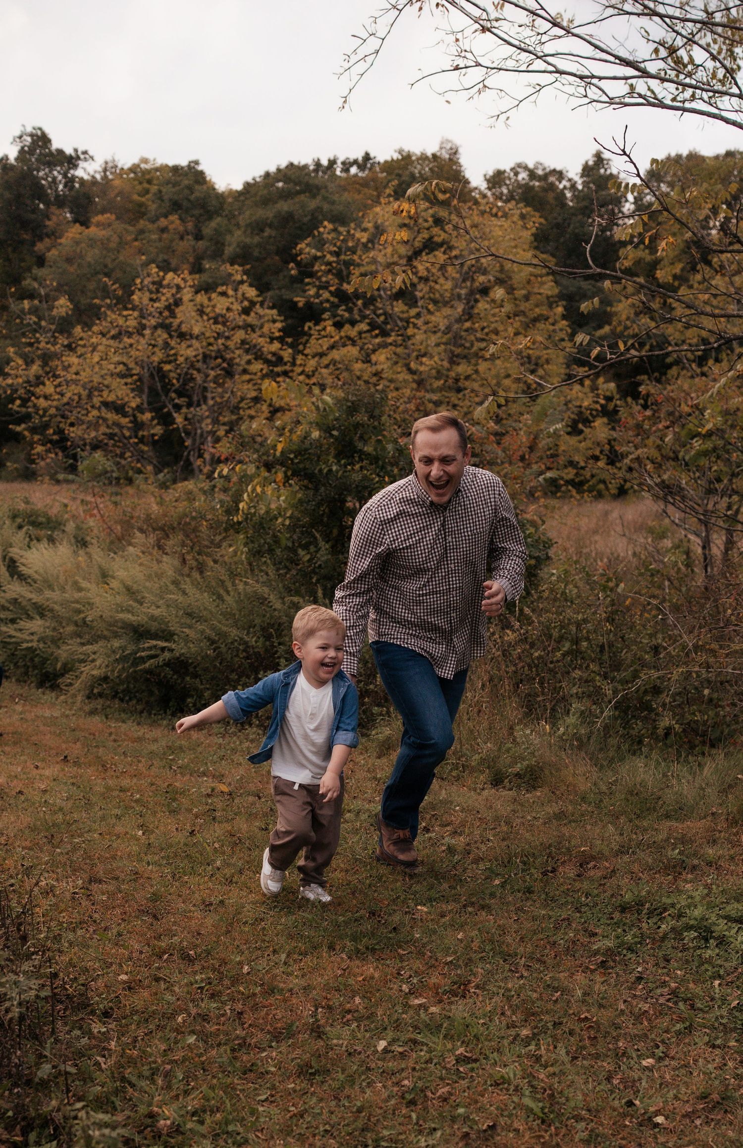 Father and toddler son laughing and running together in autumn field.