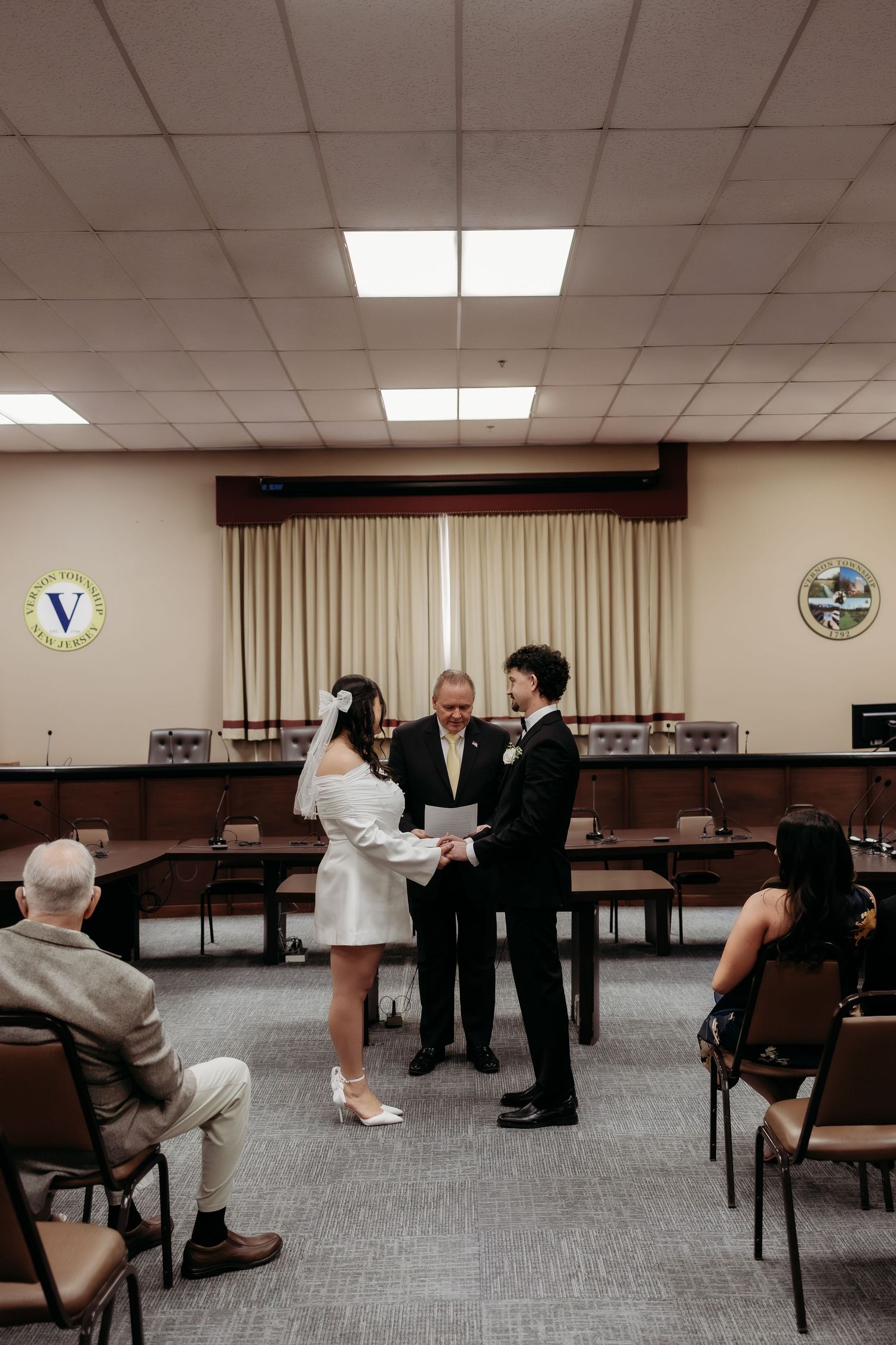 Couple exchanging vows in a courthouse wedding ceremony with an officiant and small group of guests.