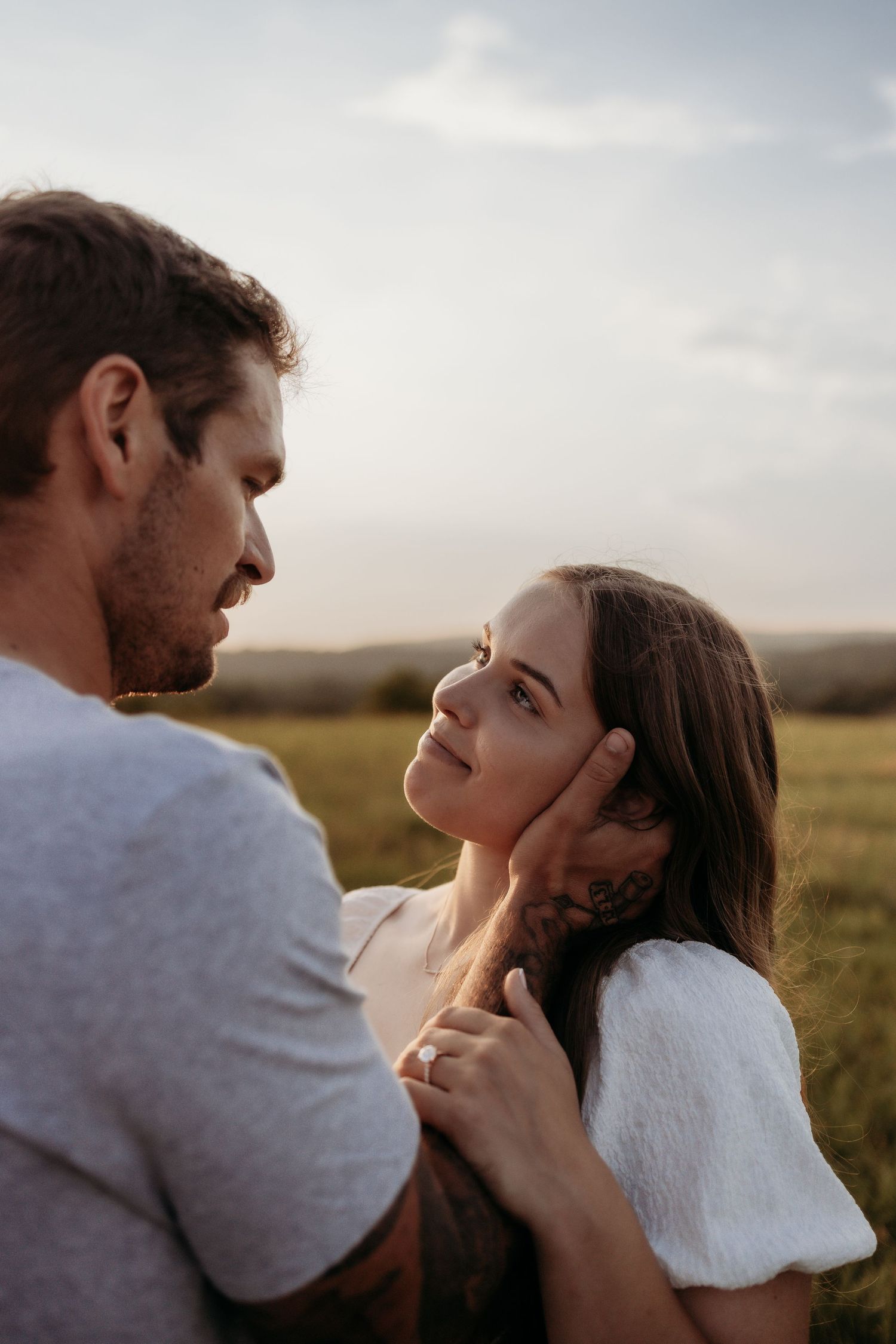 A couple shares a tender moment in a golden field, man gently cupping womans face as she gazes up at him.