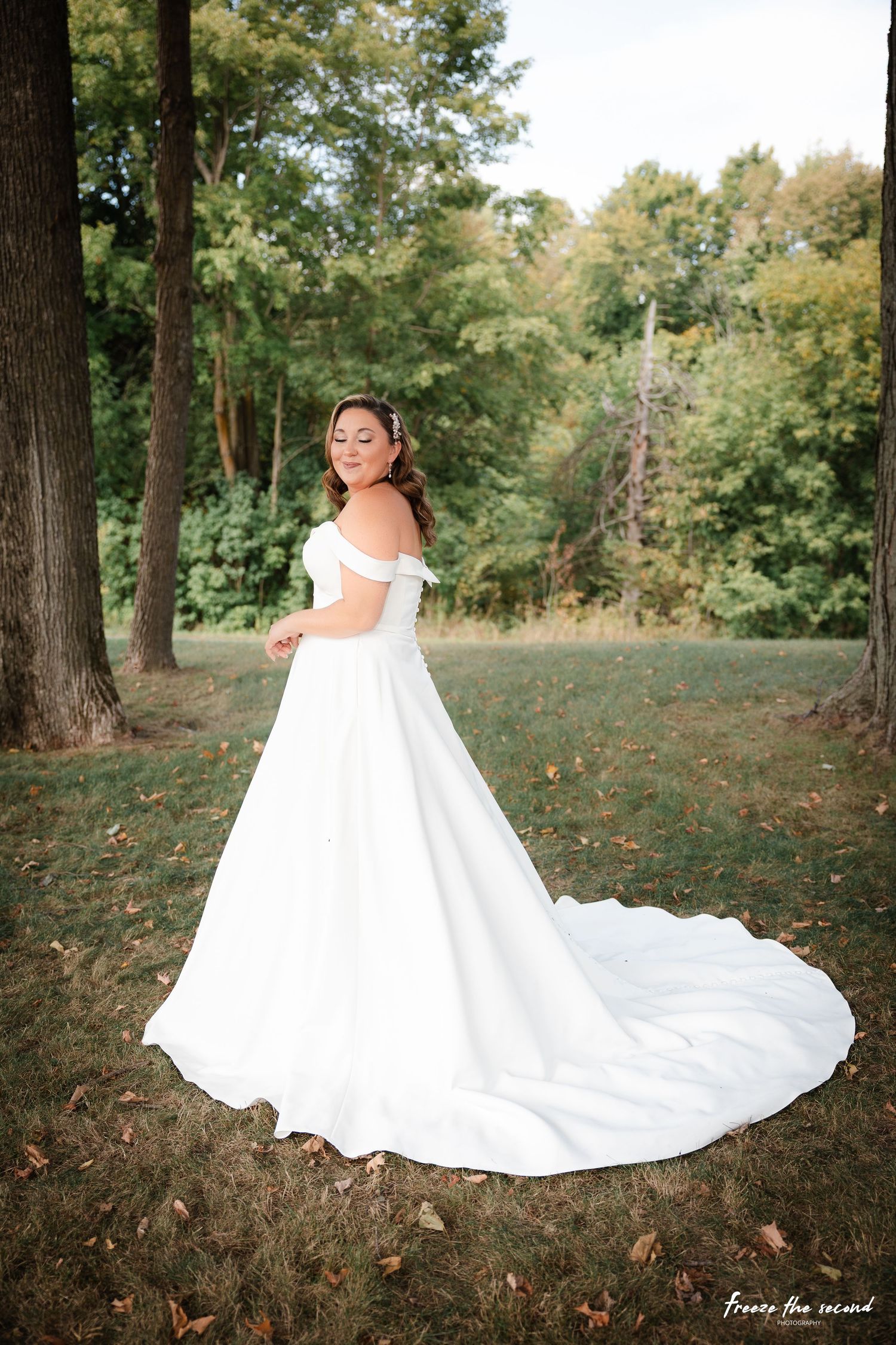 A stunning bridal portrait series in a wooded setting shows a flowing white wedding gown with dramatic train against autumn foliage.