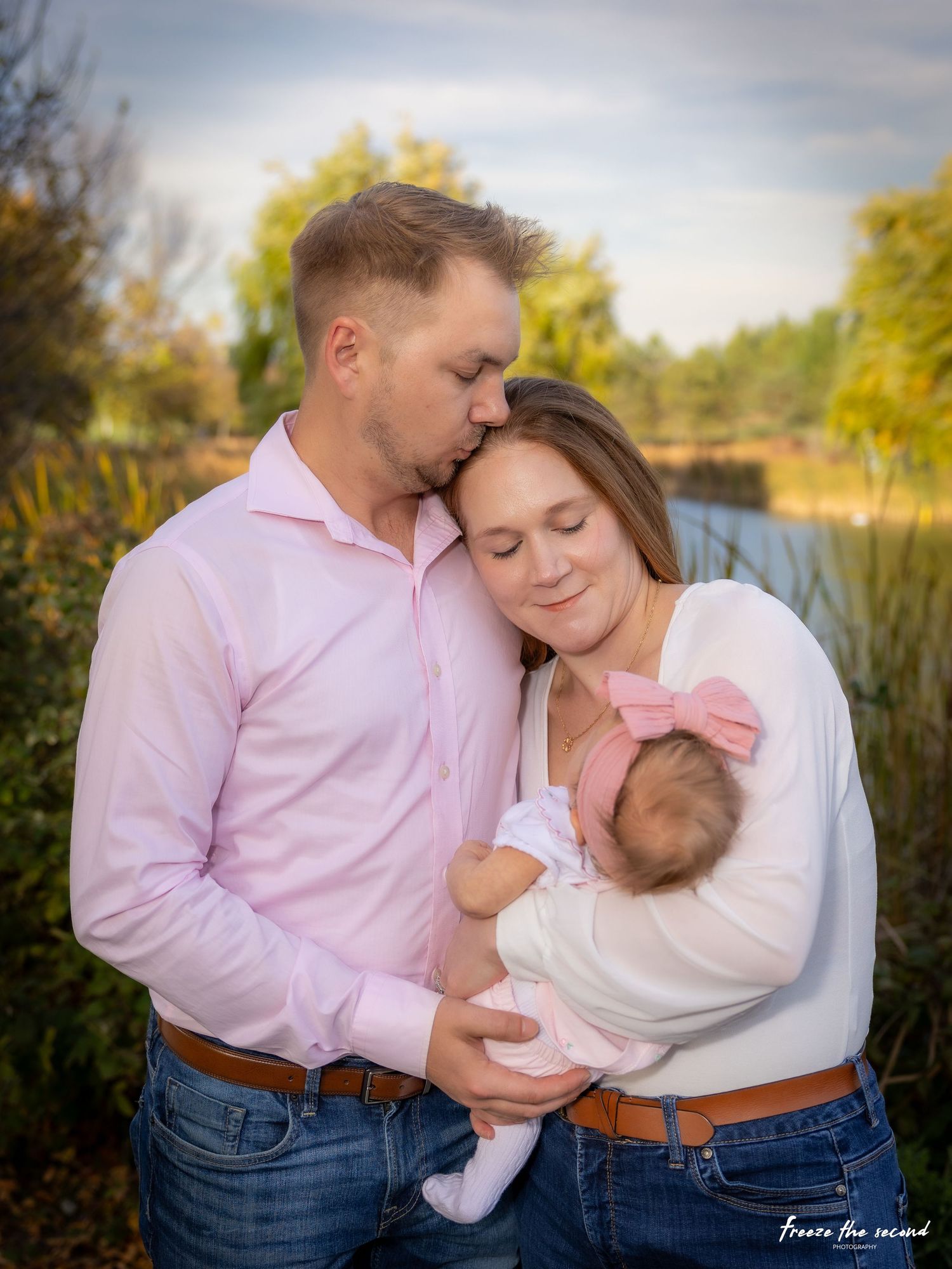 Parents in pink and white shirts share tender moment with newborn baby outdoors at dusk.