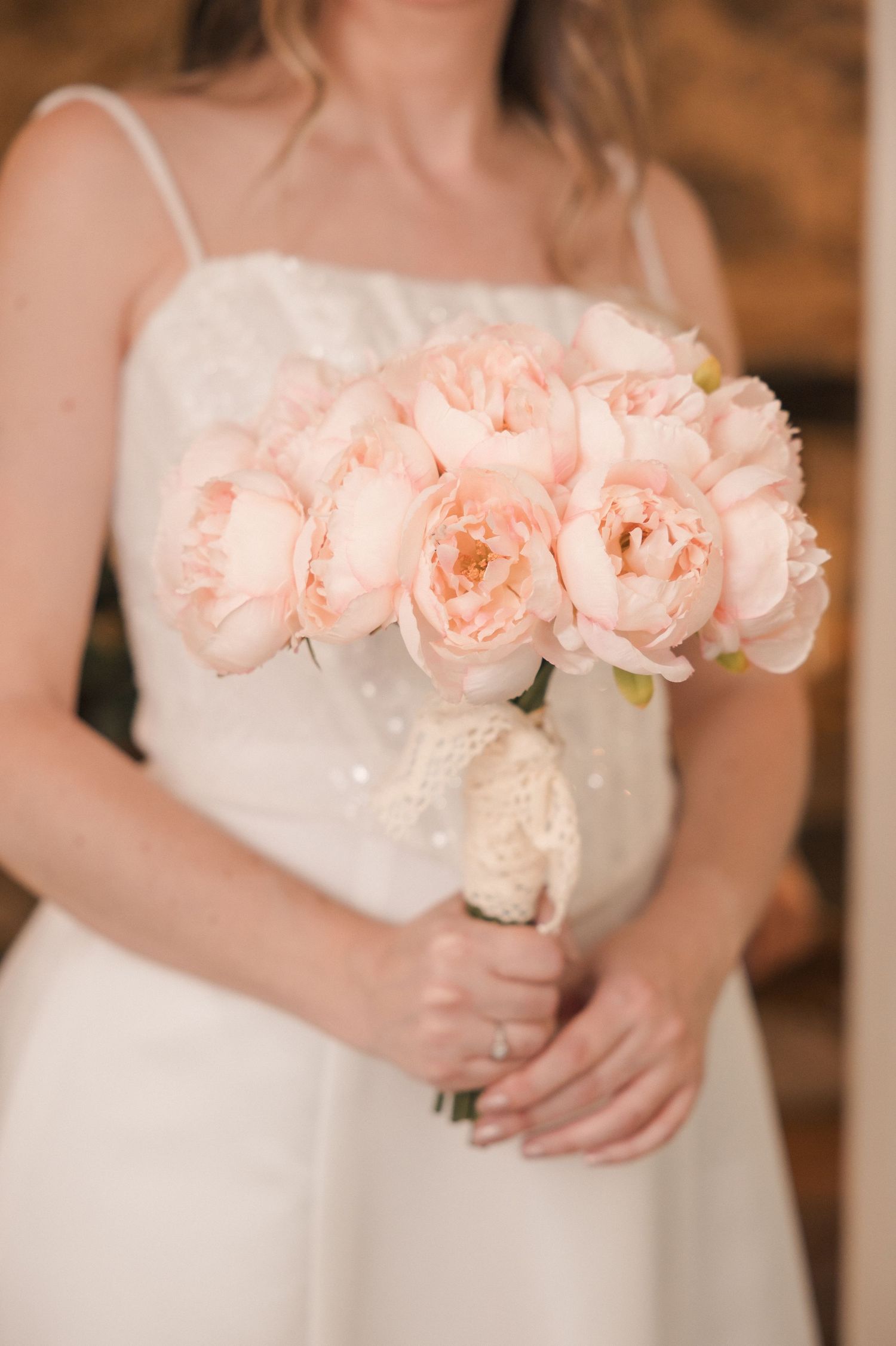 Bride holding elegant bouquet of blush pink peonies in white wedding dress.