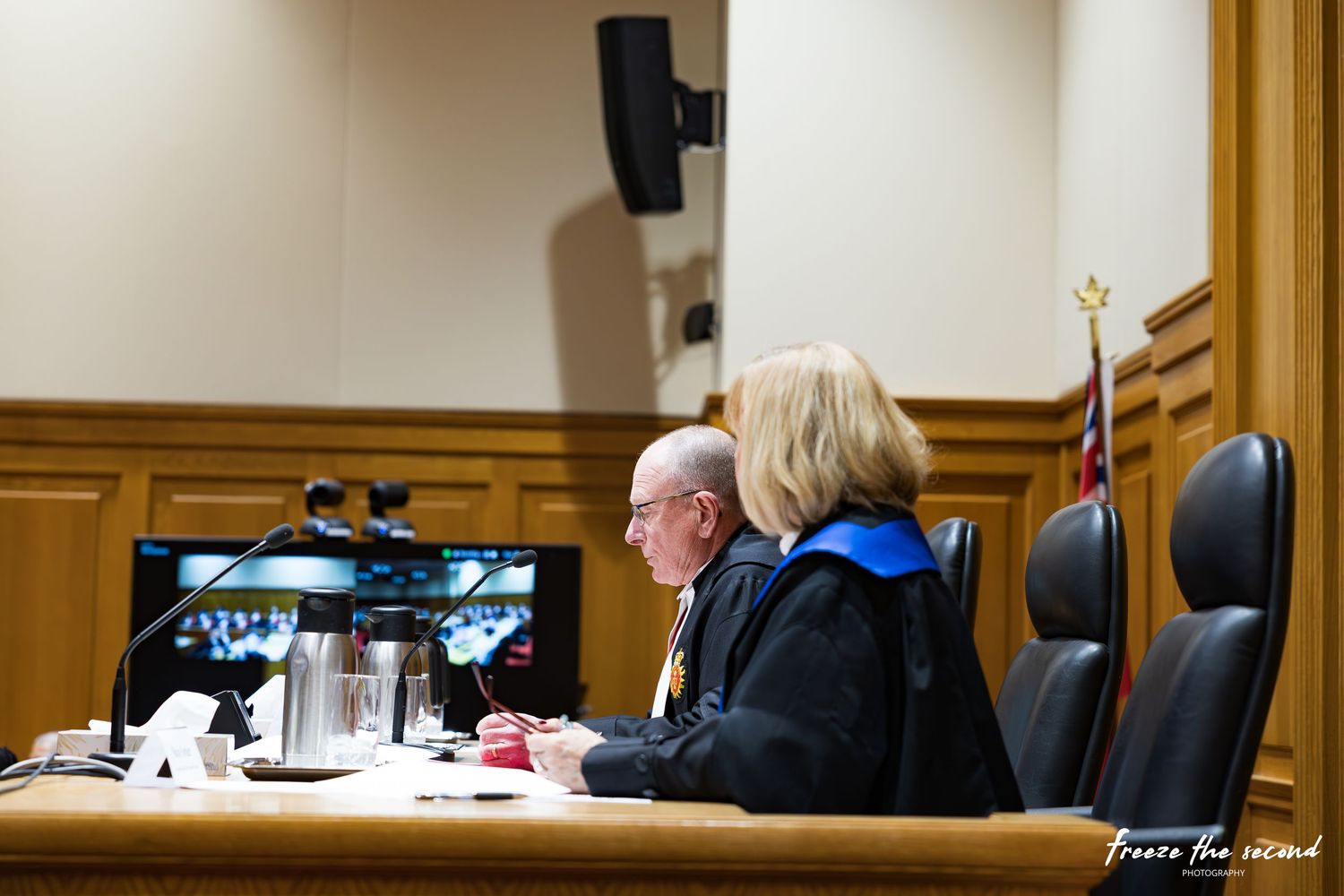 Two judges in formal robes sit at bench reviewing documents in a wood-paneled courtroom.