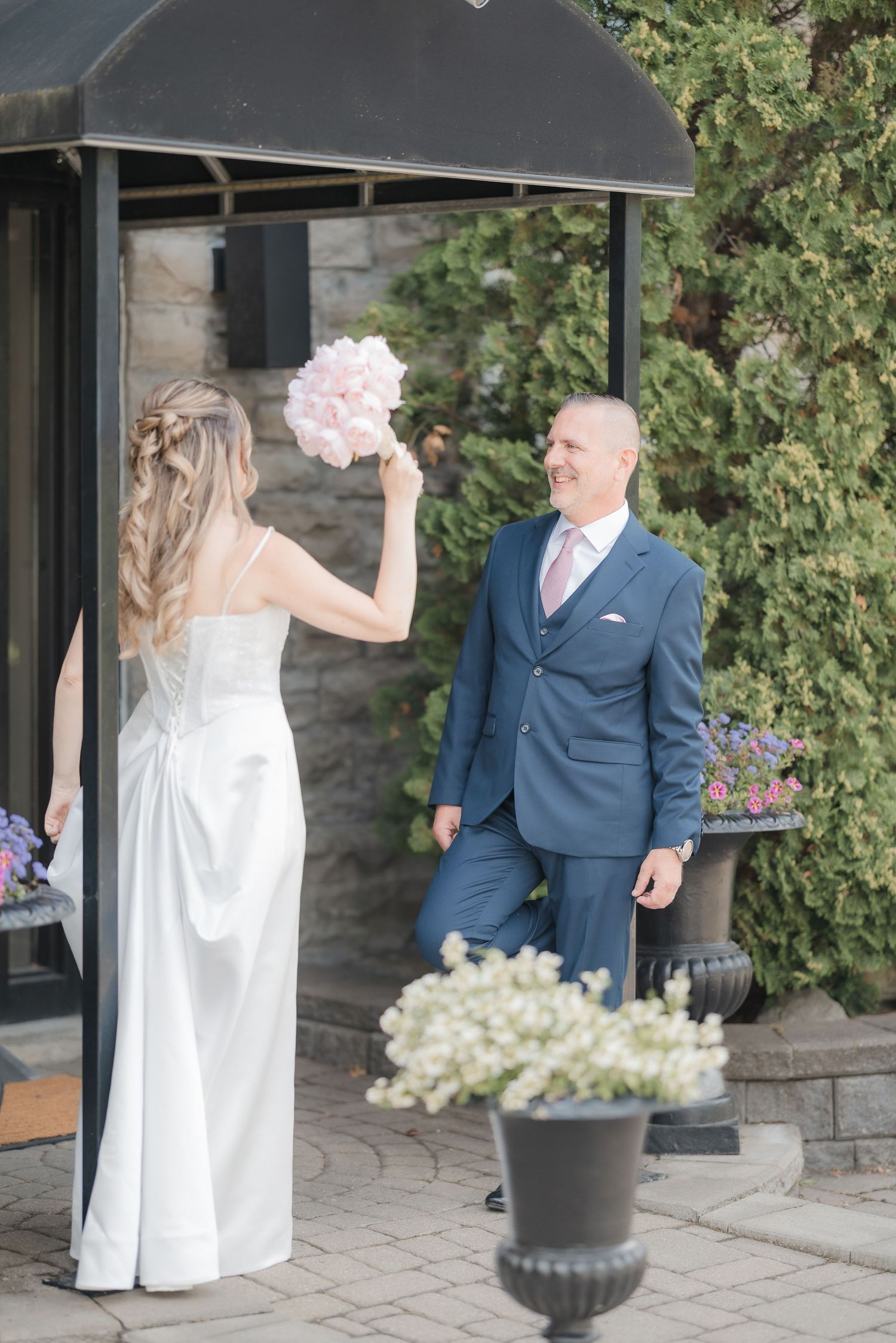 Groom in navy suit smiles at bride during first look on stone patio outdoors.