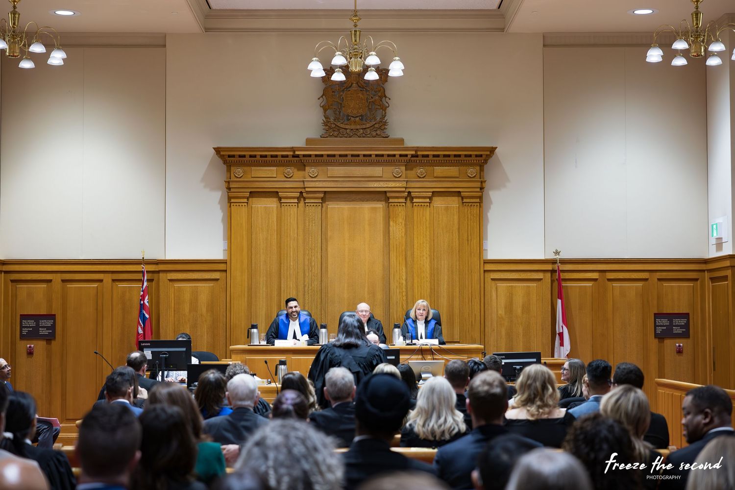 Wide view of formal courtroom ceremony with judges at bench and audience filling the gallery.