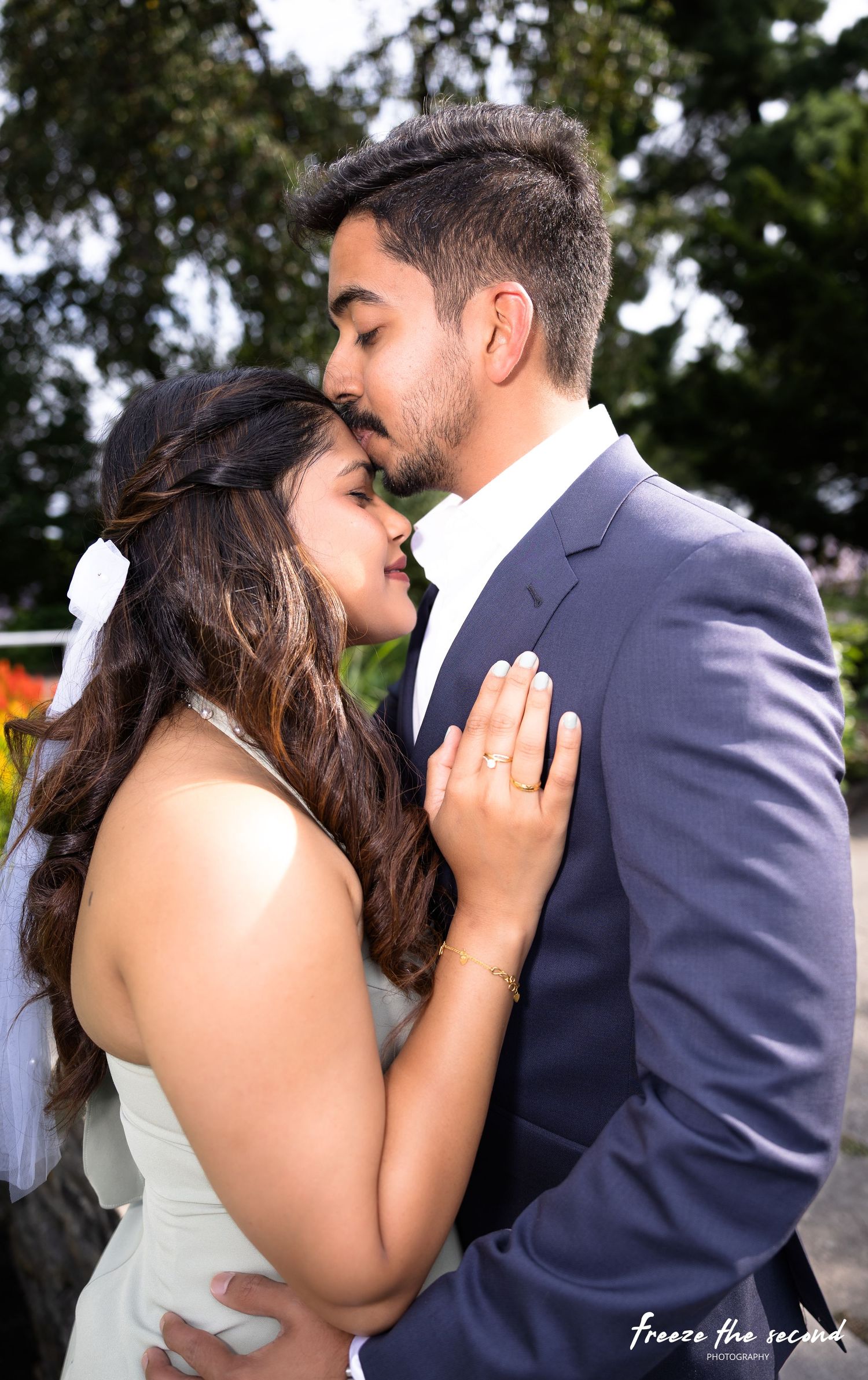 Couple sharing a tender almost-kiss moment outdoors, woman in white dress and man in navy suit.