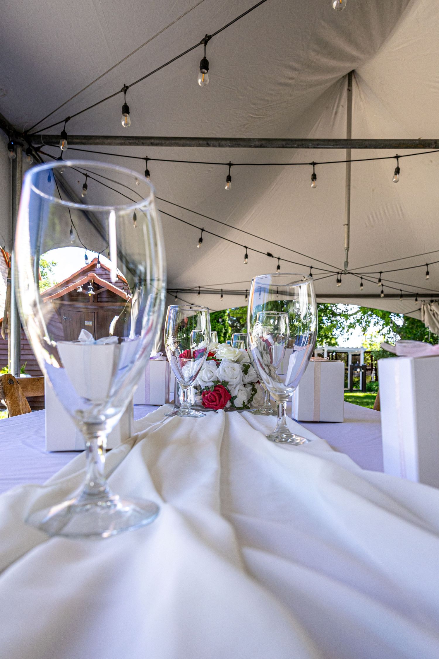 Elegant wedding reception table set with champagne flutes and floral centerpieces under a tent with string lights.