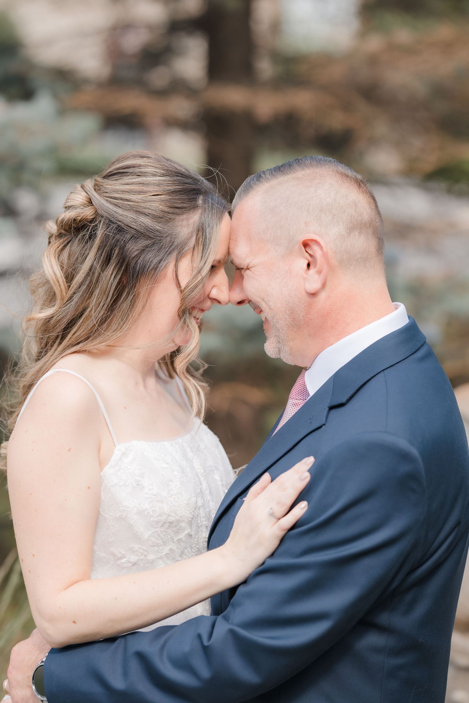 Bride and groom touching foreheads and smiling intimately during outdoor wedding portrait session.