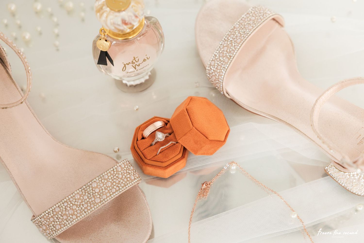 Elegant peach and blush colored wedding accessories including silk ribbons, lace details, and delicate shoes laid on white surface.