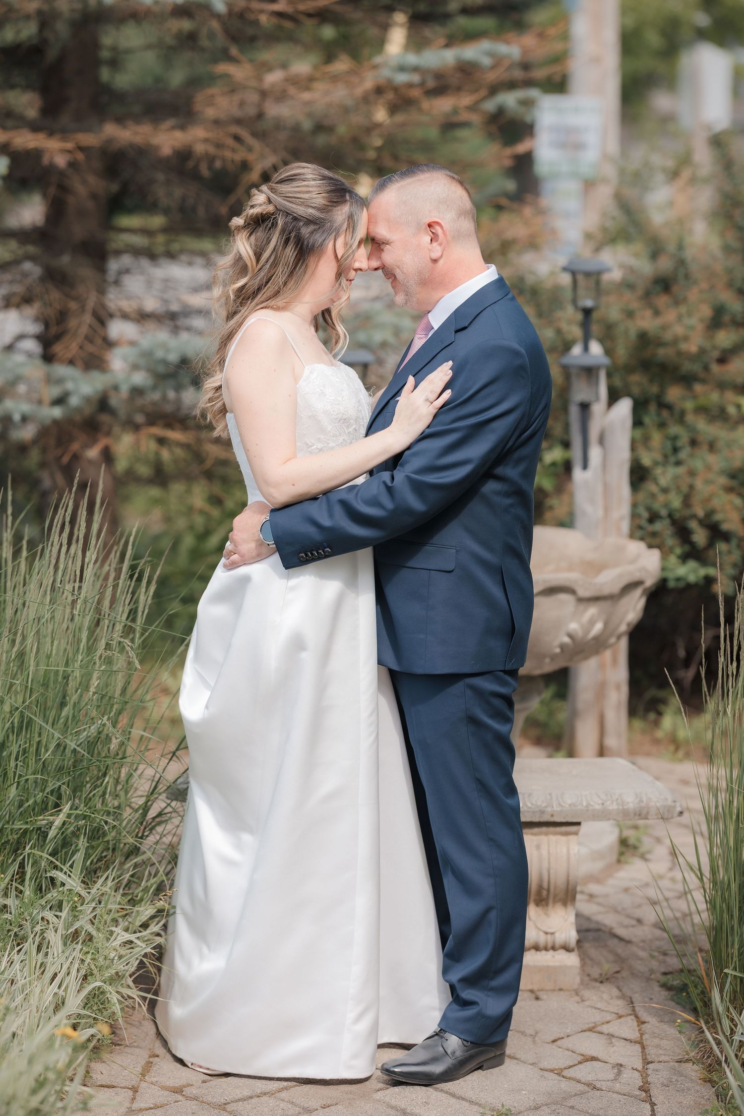Bride and groom sharing an intimate forehead touch embrace on garden stone pathway outdoors.