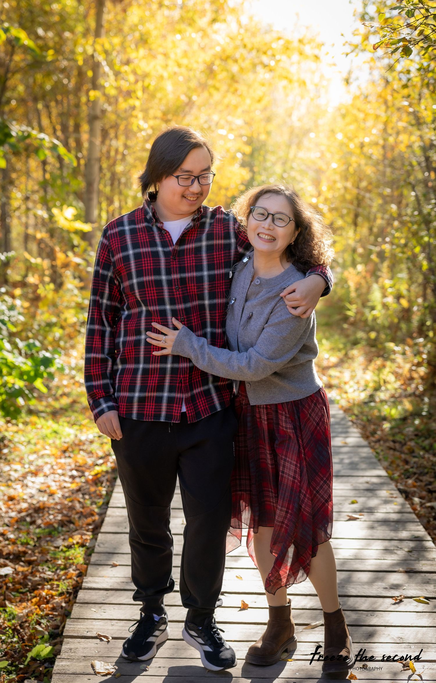 A young couple walks and laughs together on a sunny autumn boardwalk trail.