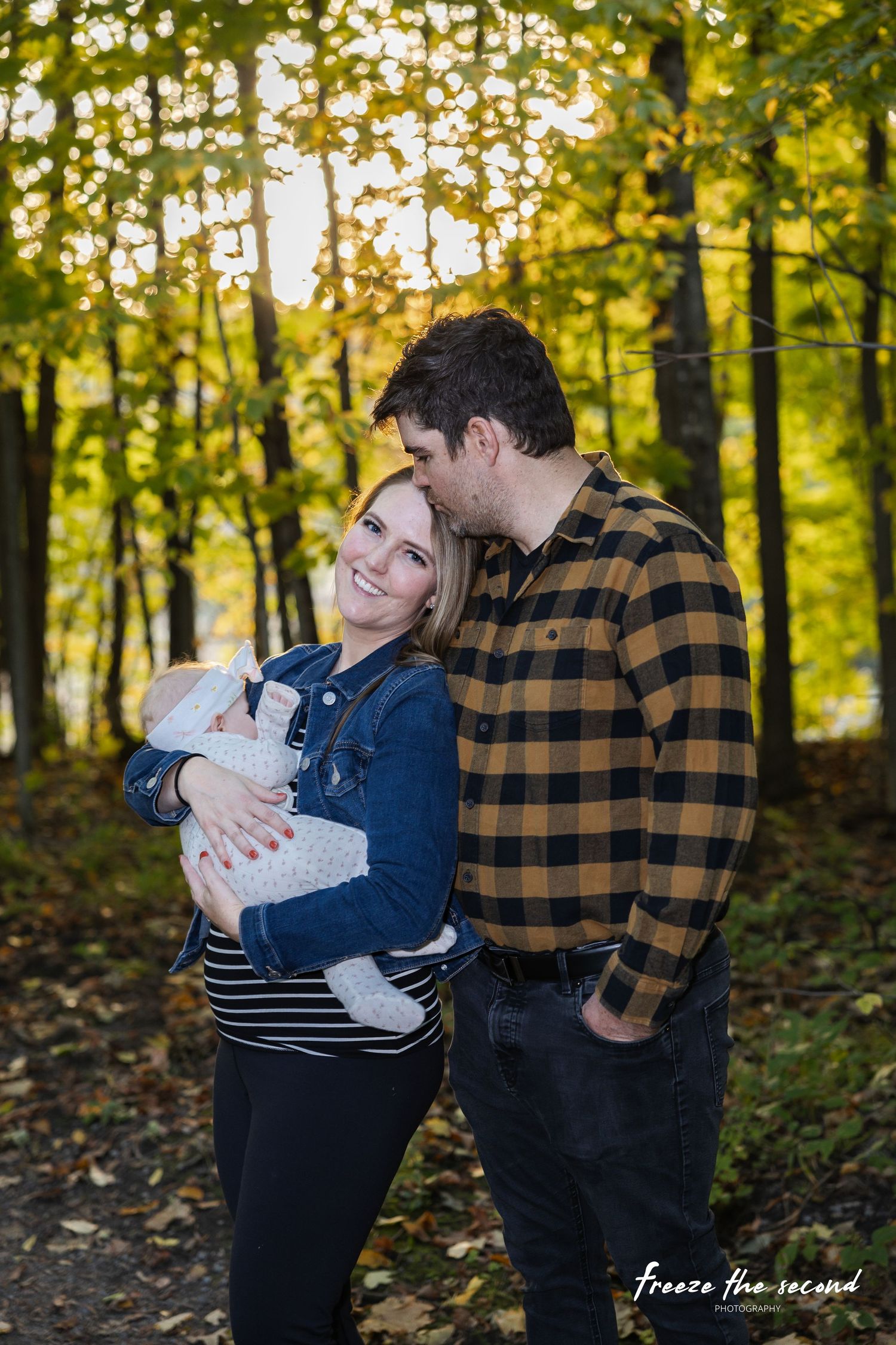 Couple with newborn baby shares tender moment during autumn family portrait in golden forest.