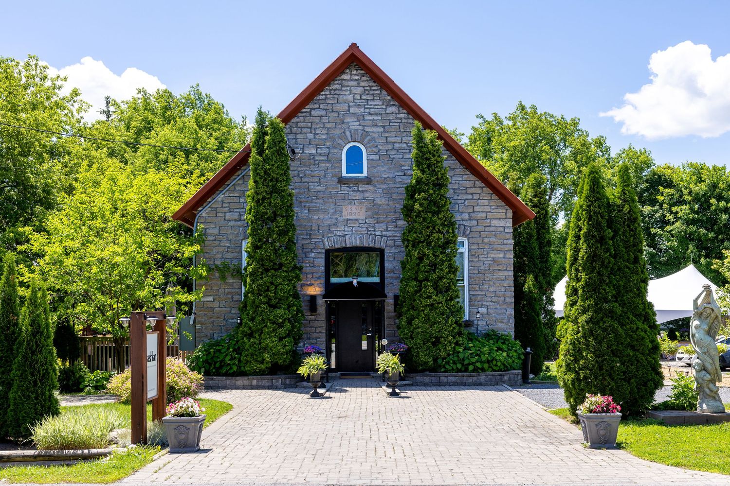 Charming stone chapel wedding venue surrounded by tall evergreen trees and lush greenery on a sunny day.