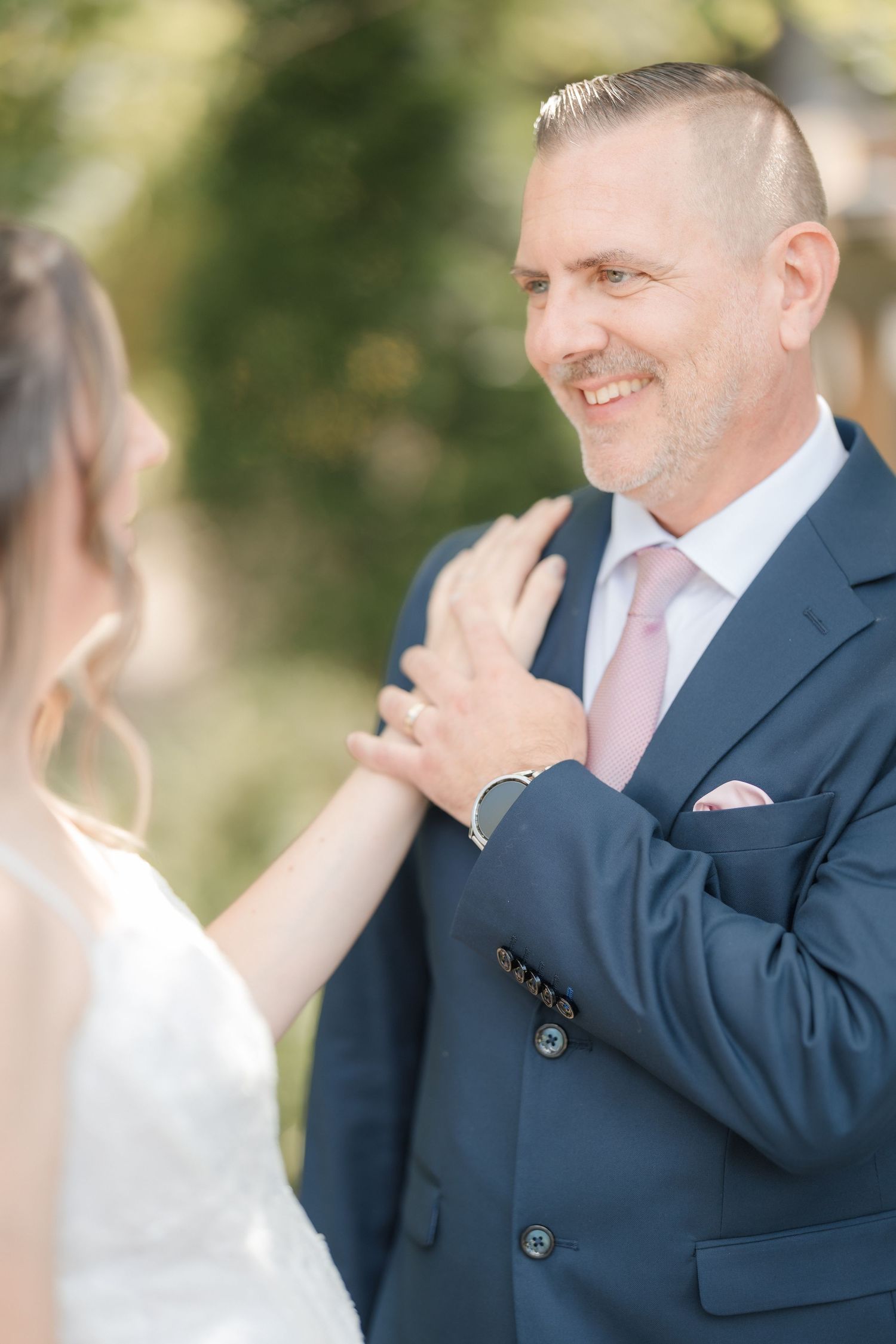 Smiling groom in navy suit with pink tie gazing at bride during outdoor wedding portraits.