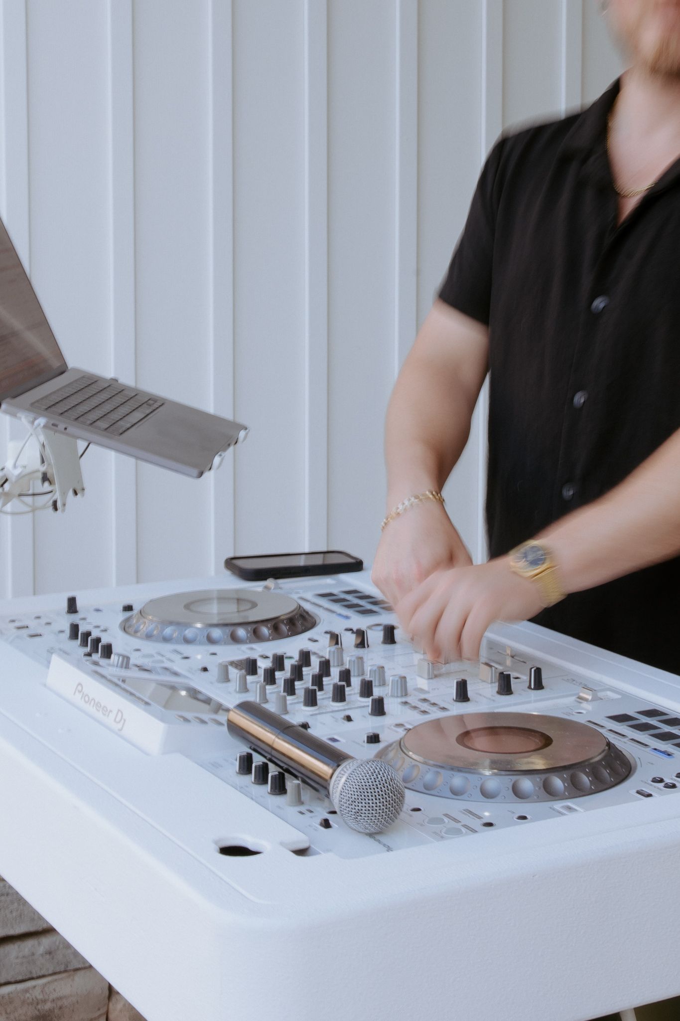 DJ mixing music on a white turntable setup with a microphone and smartphone at an event.