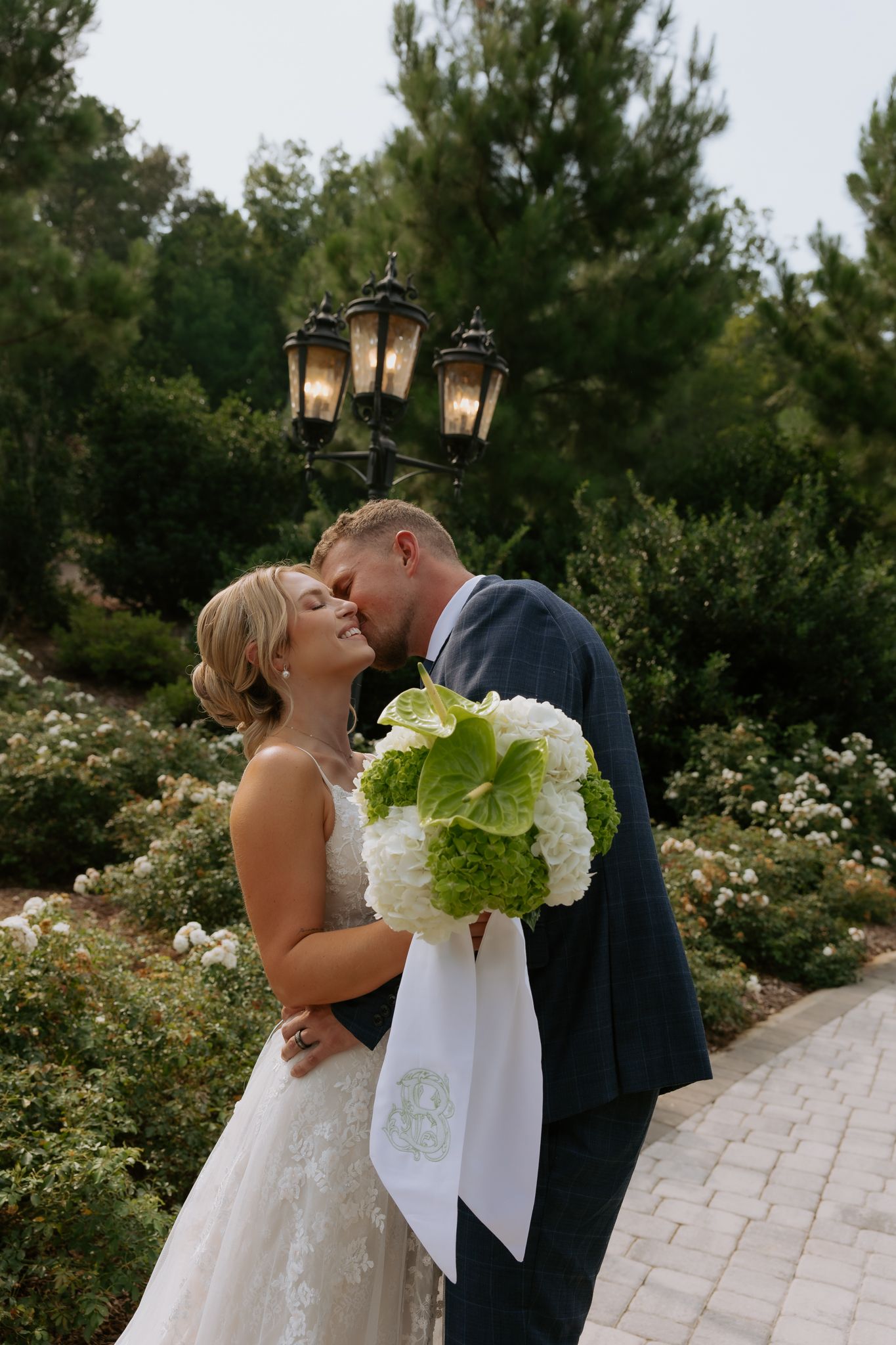 Bride and groom share a romantic kiss in a lush garden, bride holding green and white hydrangea bouquet at Heyward Manor.