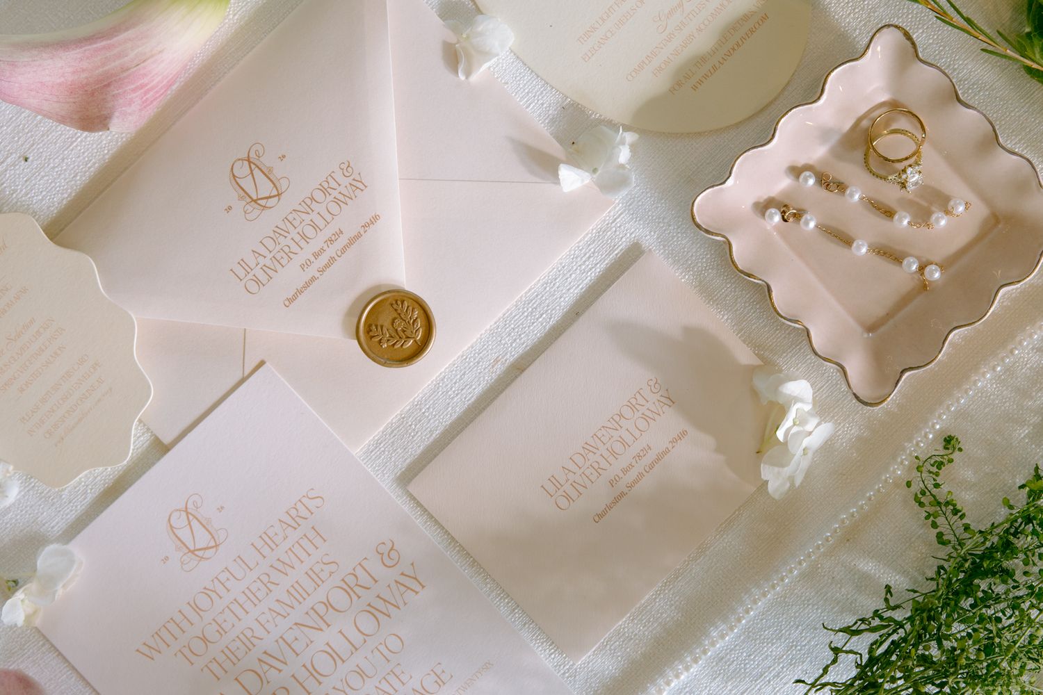 Elegant wedding stationery suite with gold wax seal, vellum envelope, and rings on white background at Heyward Manor.