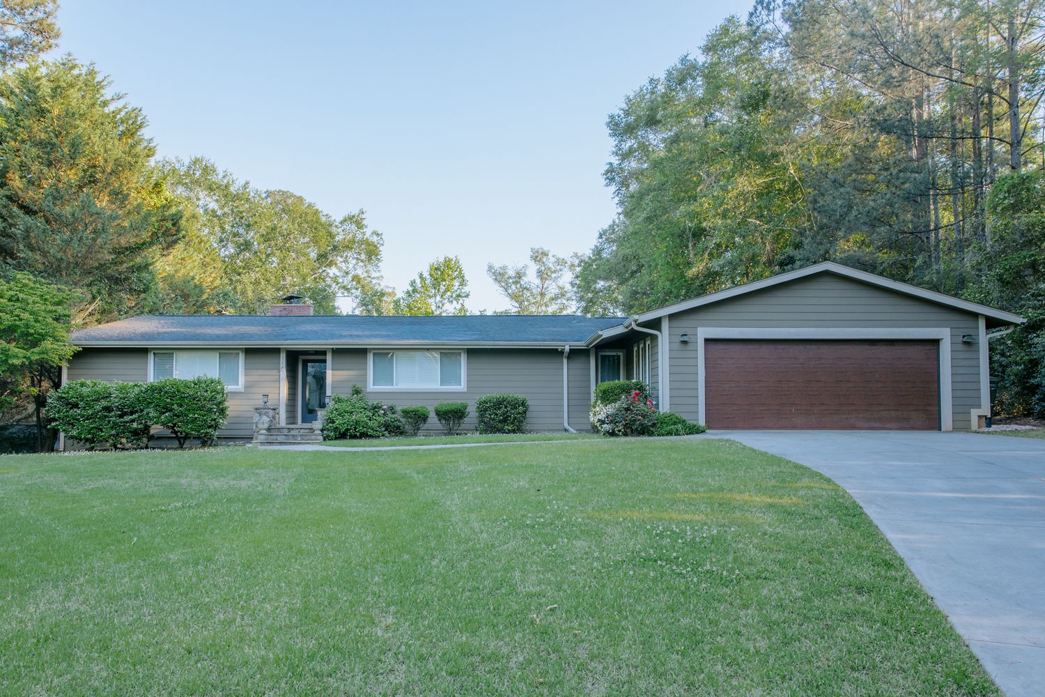 Ranch-style home with brown garage door, manicured lawn, and mature trees in background.
