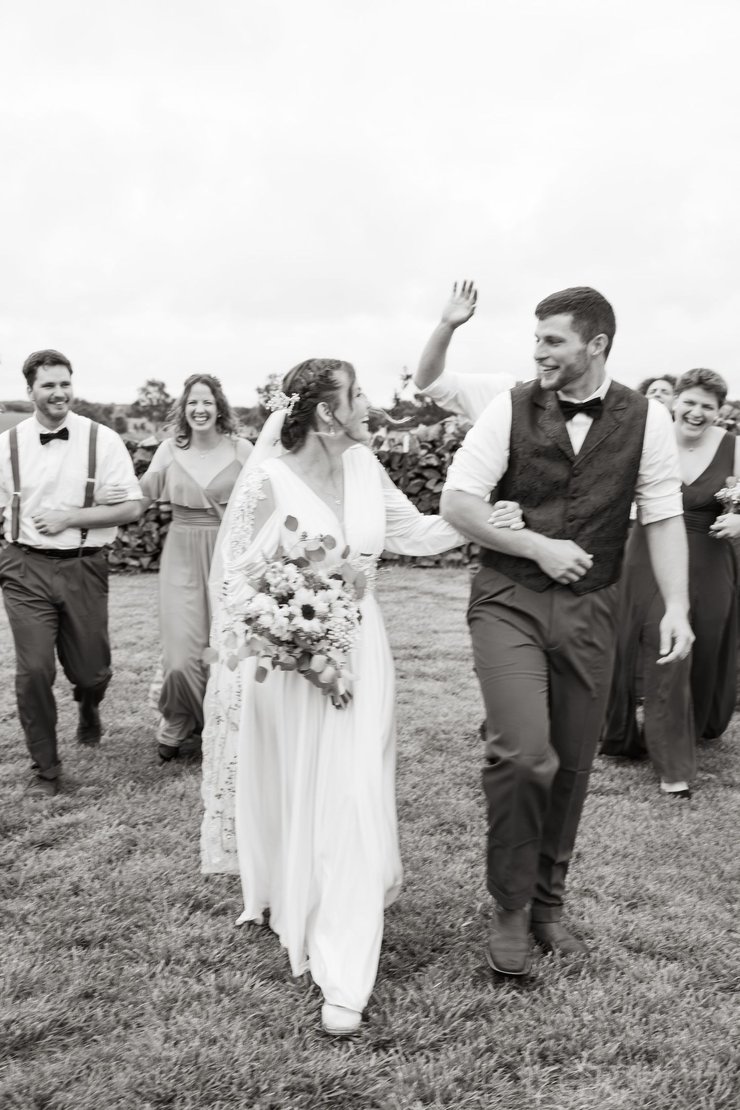 ©AnnaVonRiesenPhotography Wedding Photography | B&W image of the bride & groom walking & smiling as their bridal party cheers behind them.