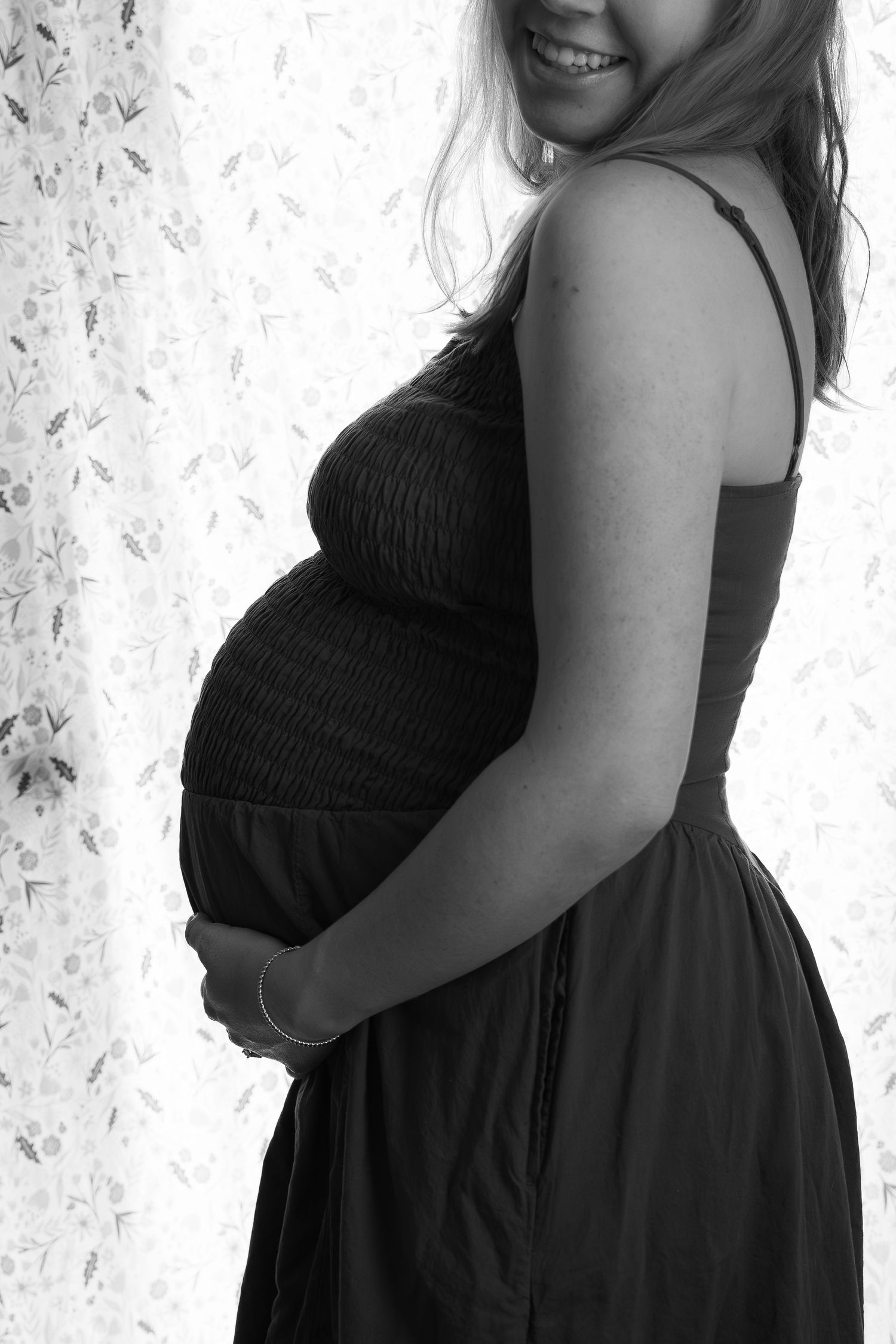 ©AnnaVonRiesenPhotography Couples Photography | B&W image of a woman smiling while holding her pregnant belly.
