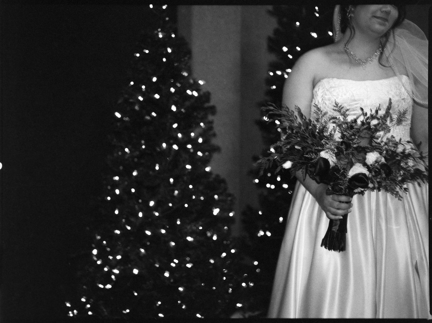 ©AnnaVonRiesenPhotography Wedding Photography | Film B&W image of the bride smiling holding her bouquet against a christmas tree.