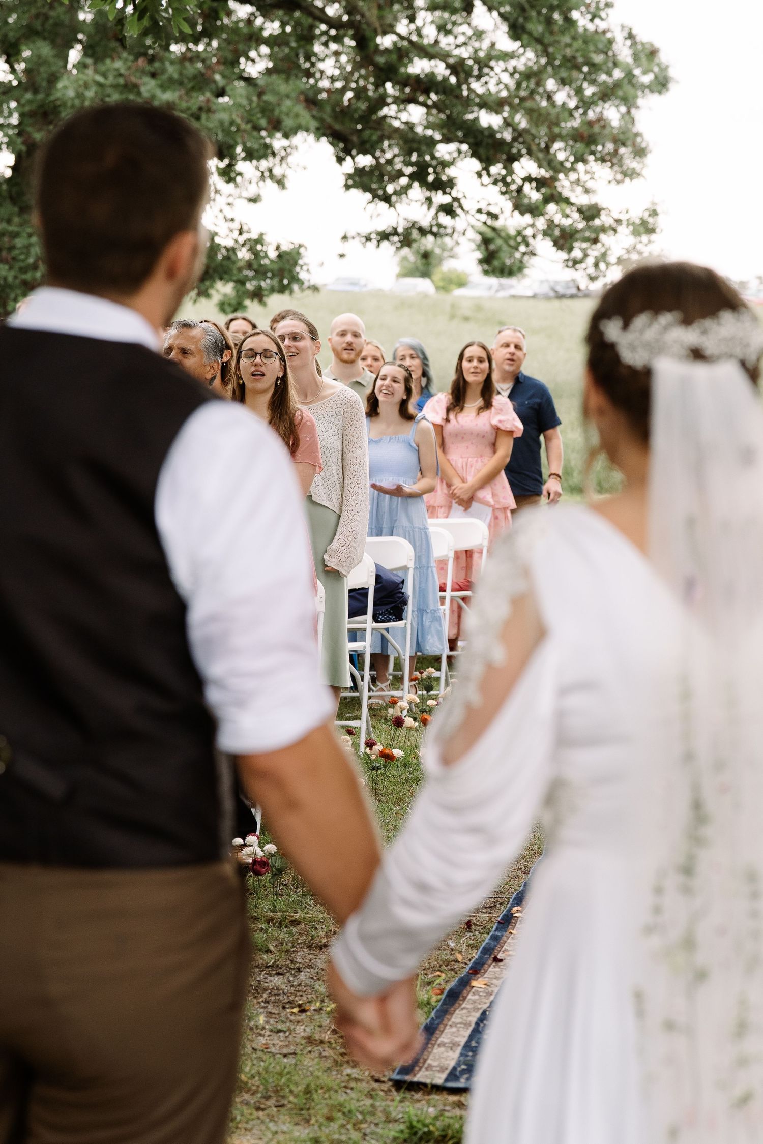 ©AnnaVonRiesenPhotography Wedding Photography | Color image of wedding guests worshipping framed by the bride & groom.