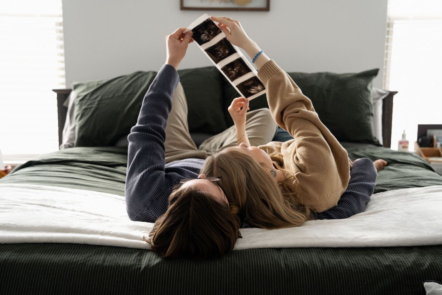 ©AnnaVonRiesenPhotography Couples Photography | Color image of a couple looking at their baby's ultrasound pictures while on the bed.