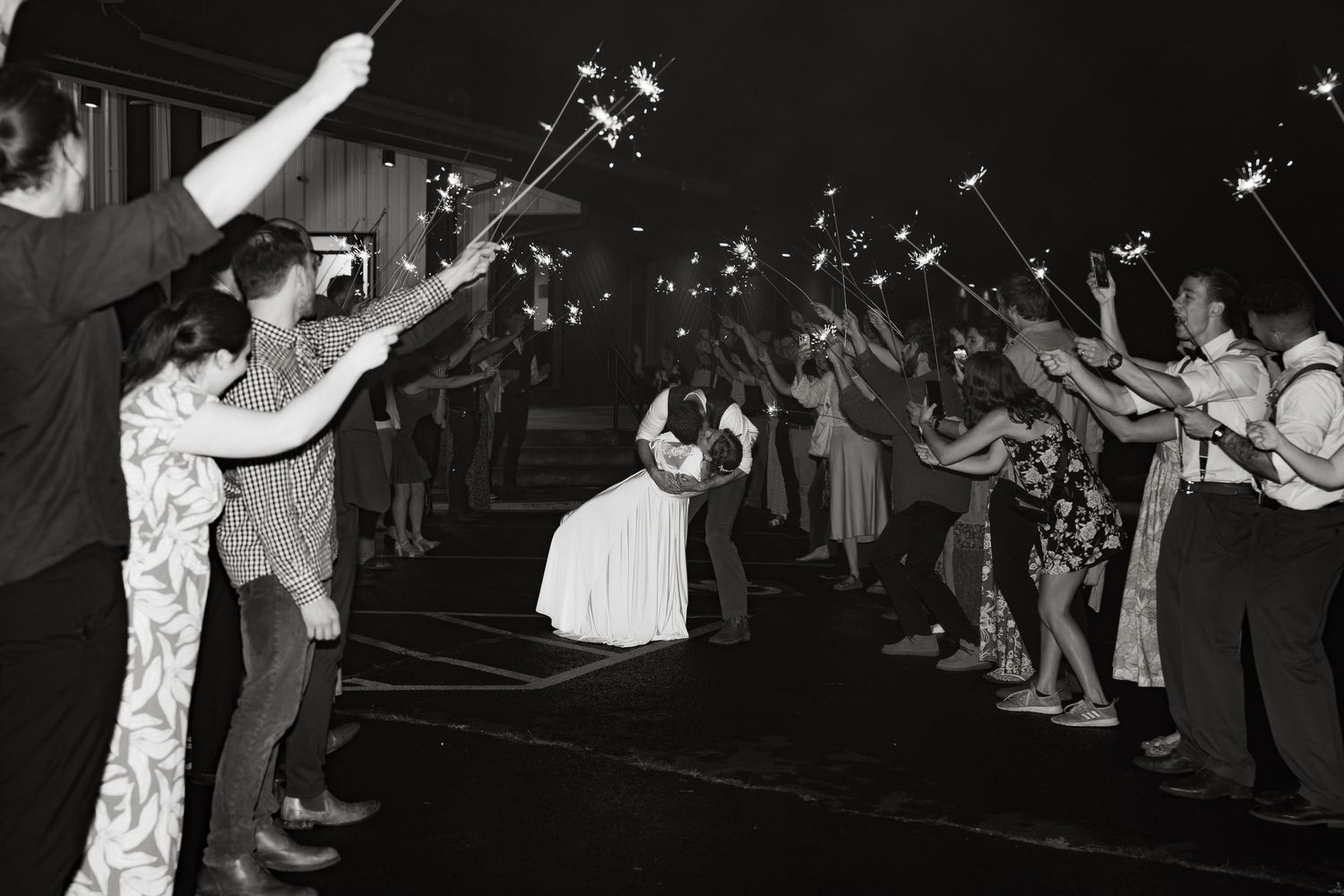 ©AnnaVonRiesenPhotography Wedding Photography | B&W image of the bride & groom dip kissing with people waving sparklers around them.