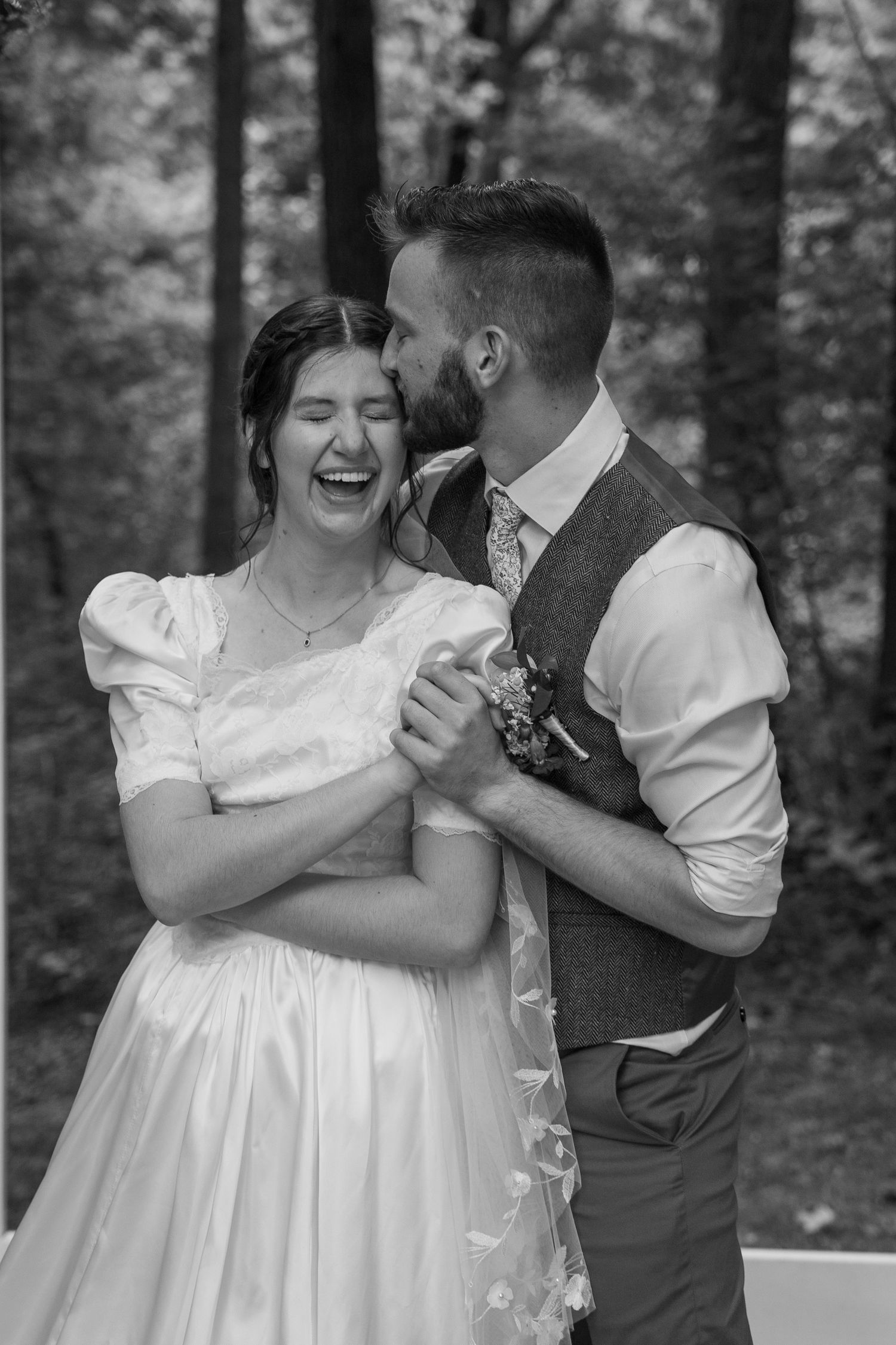 ©AnnaVonRiesenPhotography Wedding Photography | B&W image of the groom kissing his bride on the temple as she laughs.