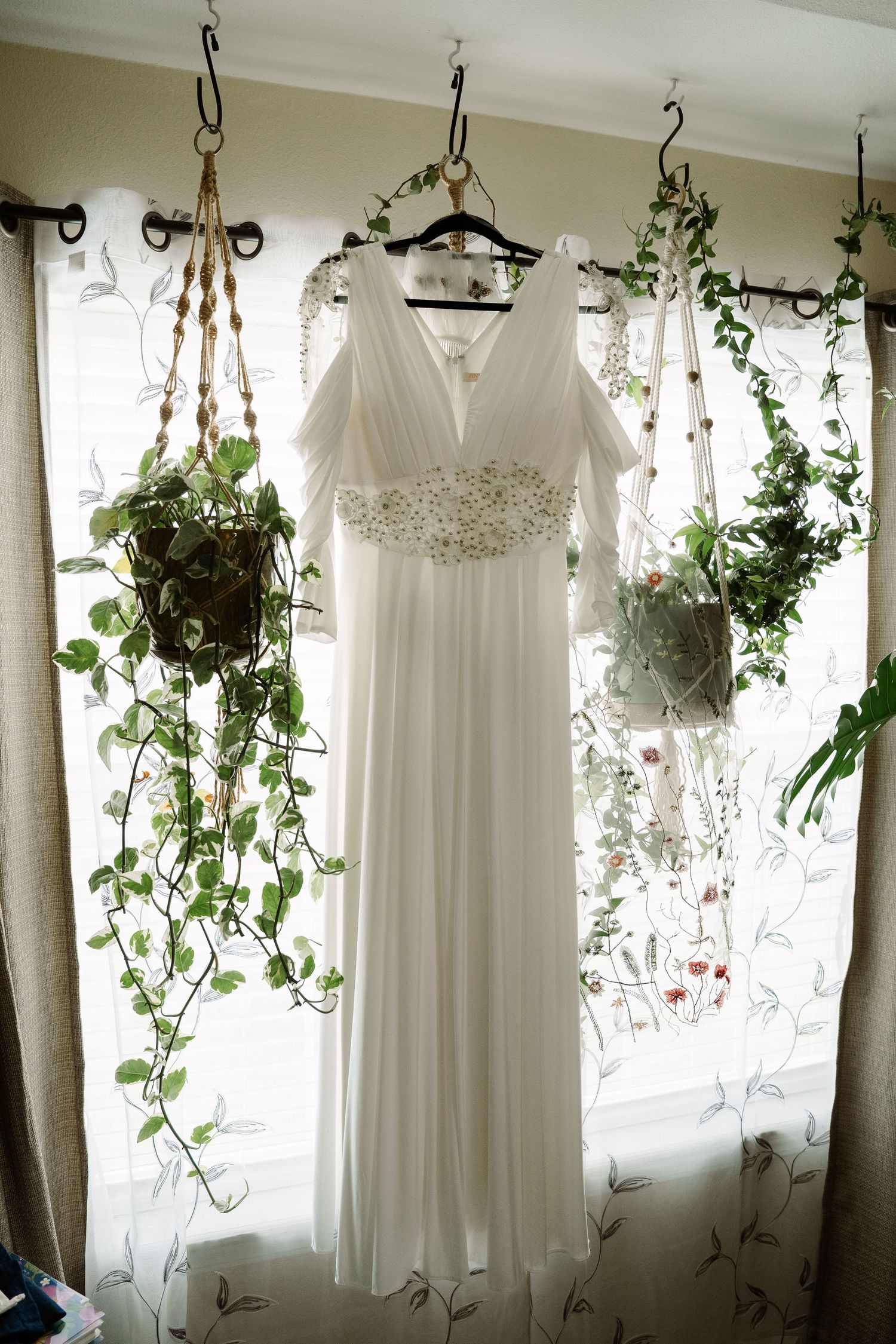 ©AnnaVonRiesenPhotography Wedding Photography | Color image of the wedding dress hanging in a window surrounded by plants.