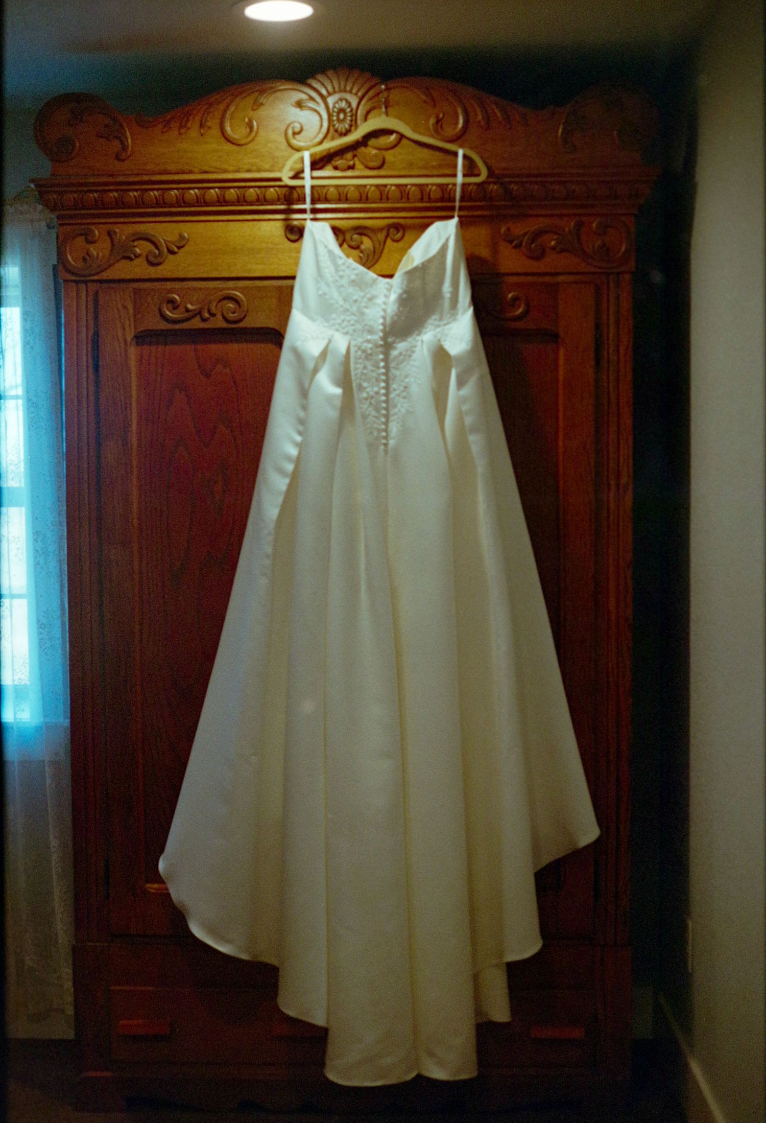 ©AnnaVonRiesenPhotography Wedding Photography | Film Color image of the wedding dress hanging on a wardrobe.