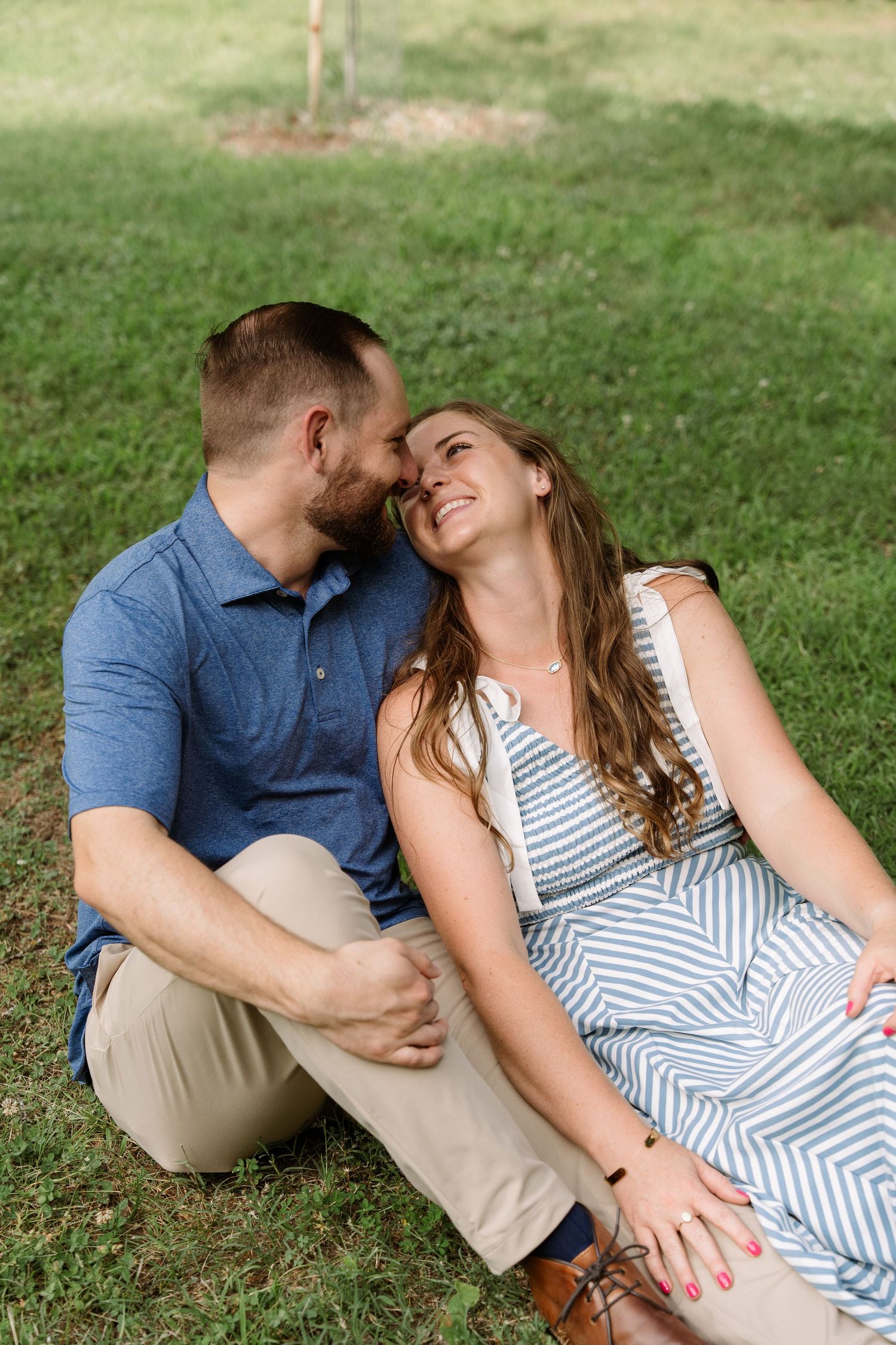 ©AnnaVonRiesenPhotography Engagement Photography | Color image of a couple sitting in the grass, the man holds his fianceé.