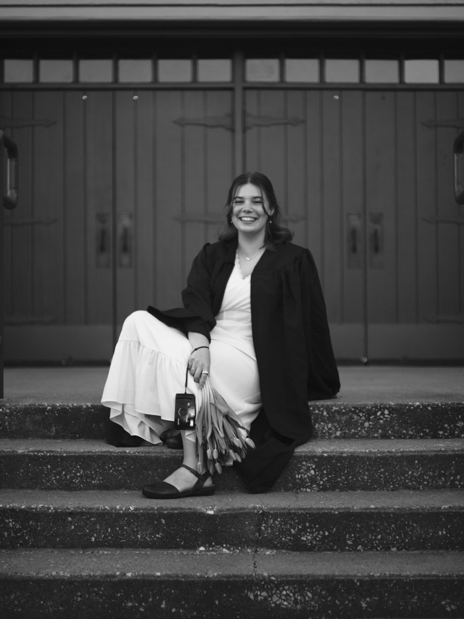 ©Stone Robinson | B&W photo of Anna VonRiesen smiling while sitting and hold a bundle of tulips.