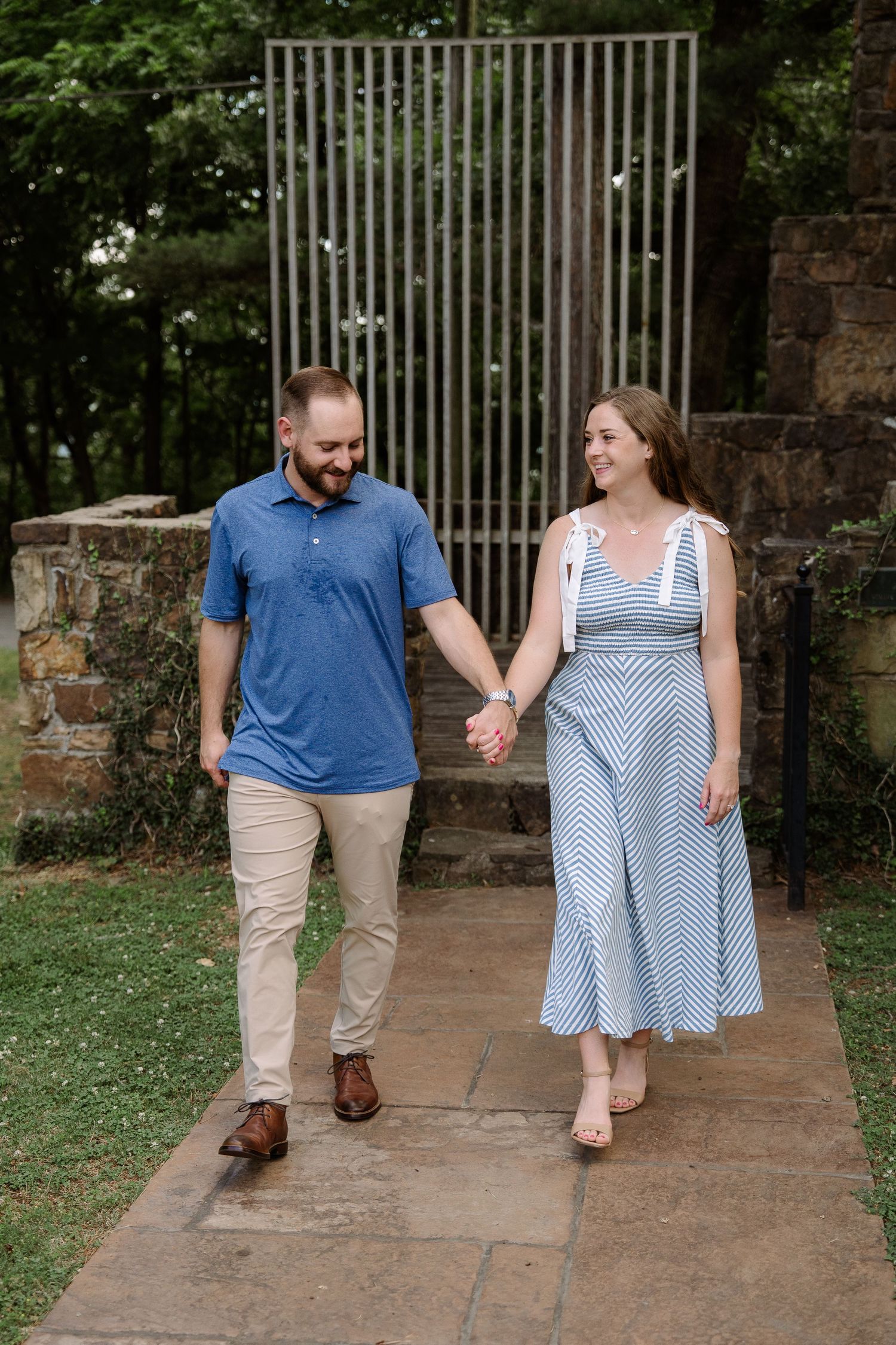 ©AnnaVonRiesenPhotography Engagement Photography | Color image of a couple walking hand in hand down a walkway.
