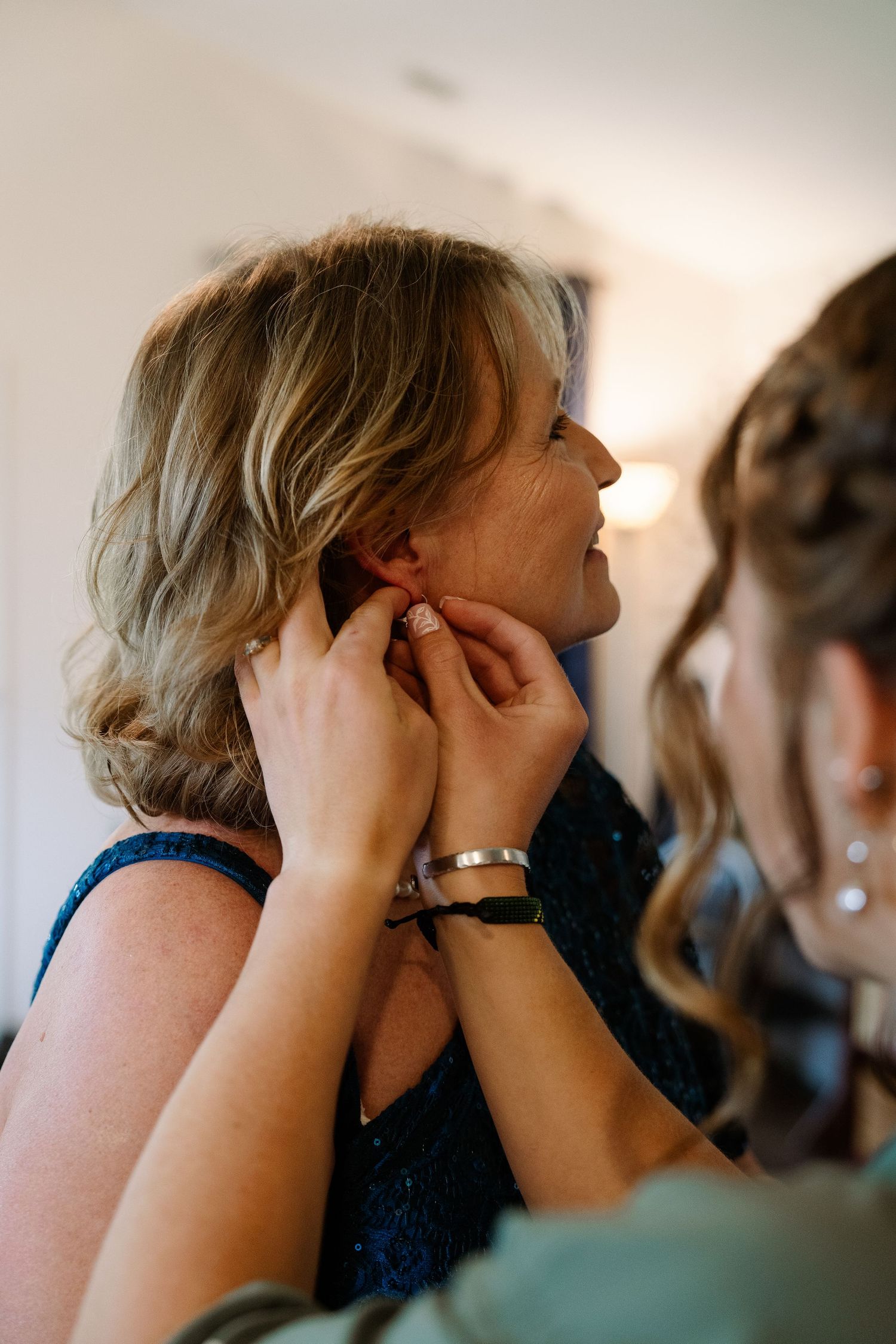 ©AnnaVonRiesenPhotography Wedding Photography | Color image of the bride's mother getting earrings put in by a bridesmaid.