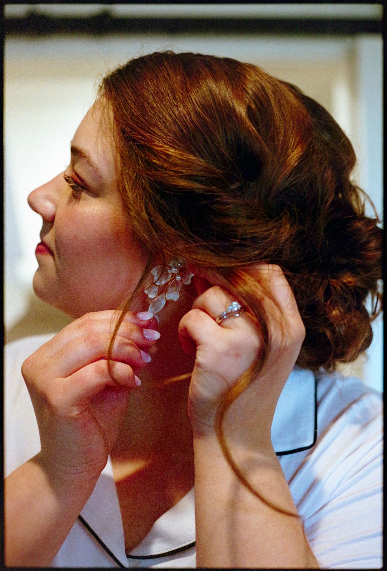 ©AnnaVonRiesenPhotography Wedding Photography | Film Color image of the bride putting on her earrings.