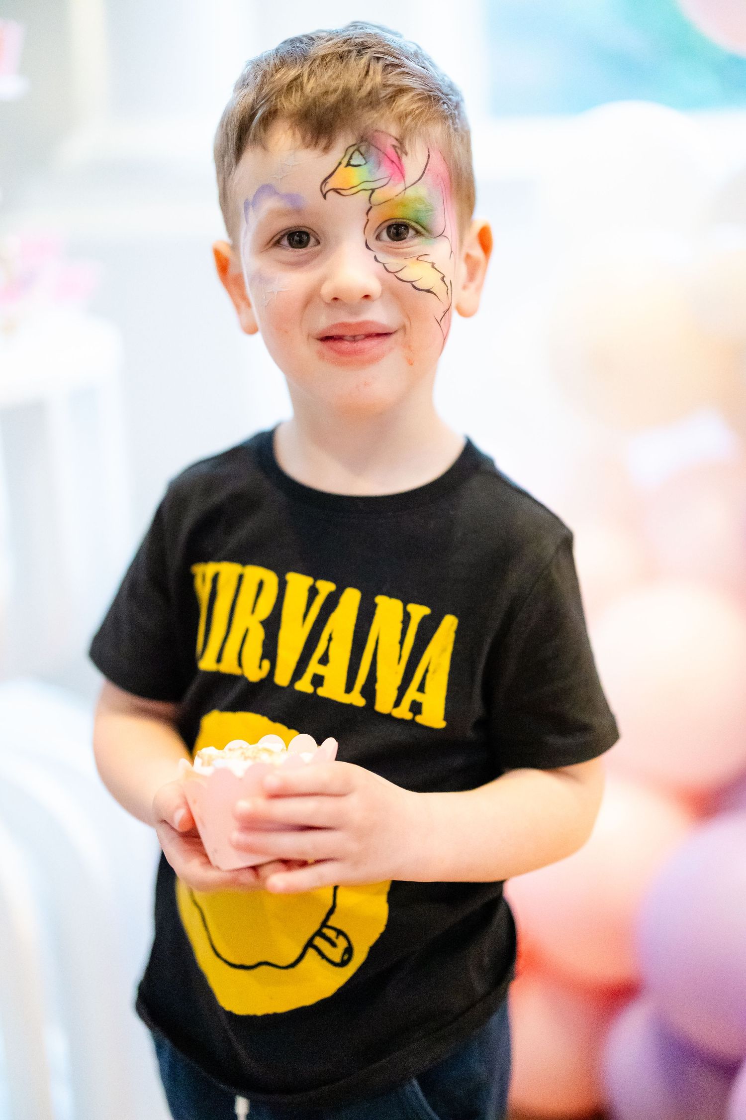 Young boy with colorful face paint wearing a Nirvana t-shirt at a birthday party.