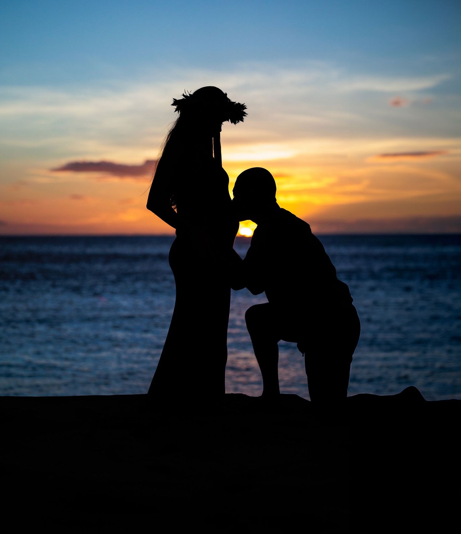 Silhouette of a couple at sunset on the beach, man kneeling before pregnant woman.