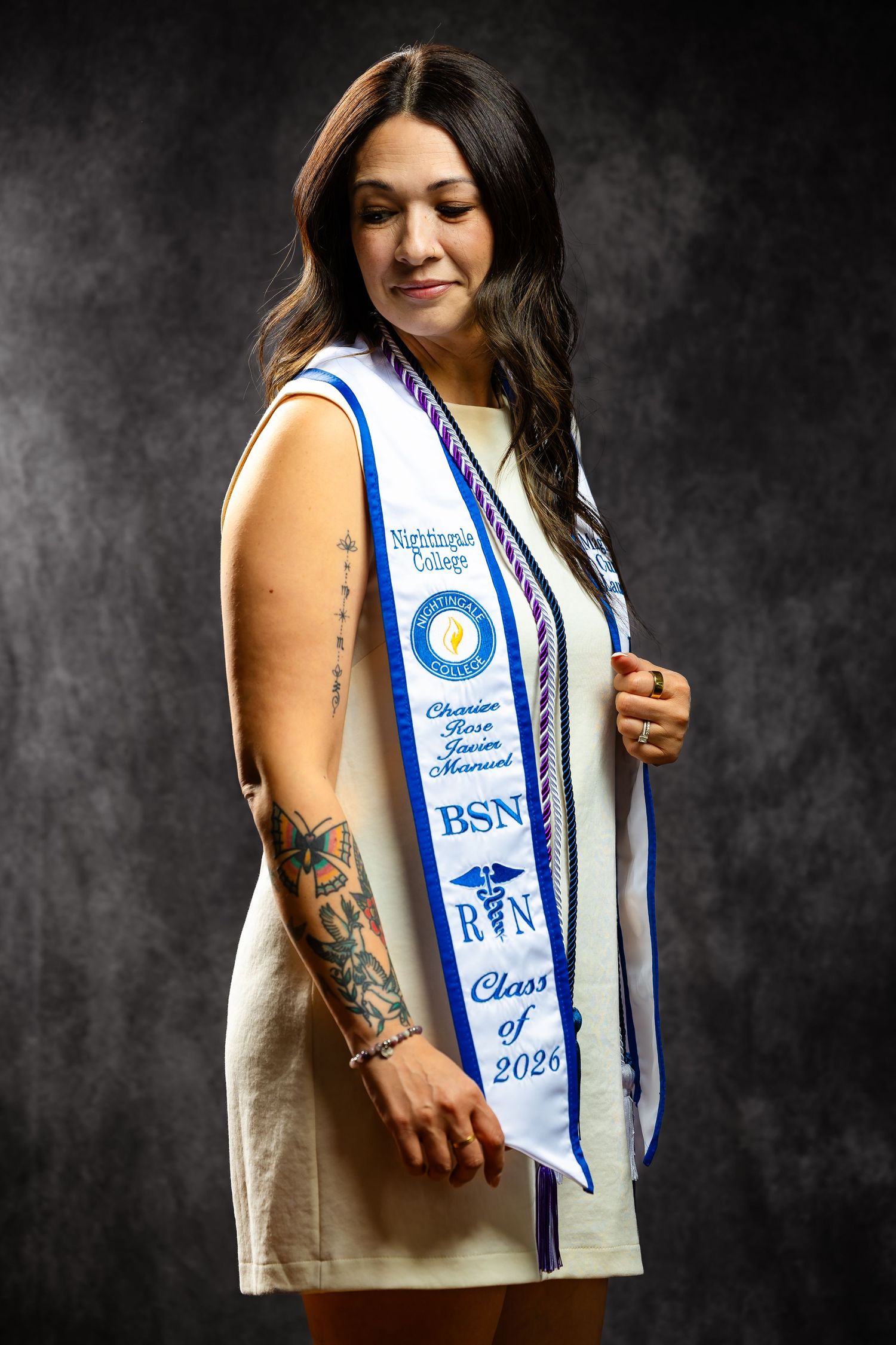 Woman wearing BSN RN Class of 2026 graduation sash from Nightingale College with tattoos.