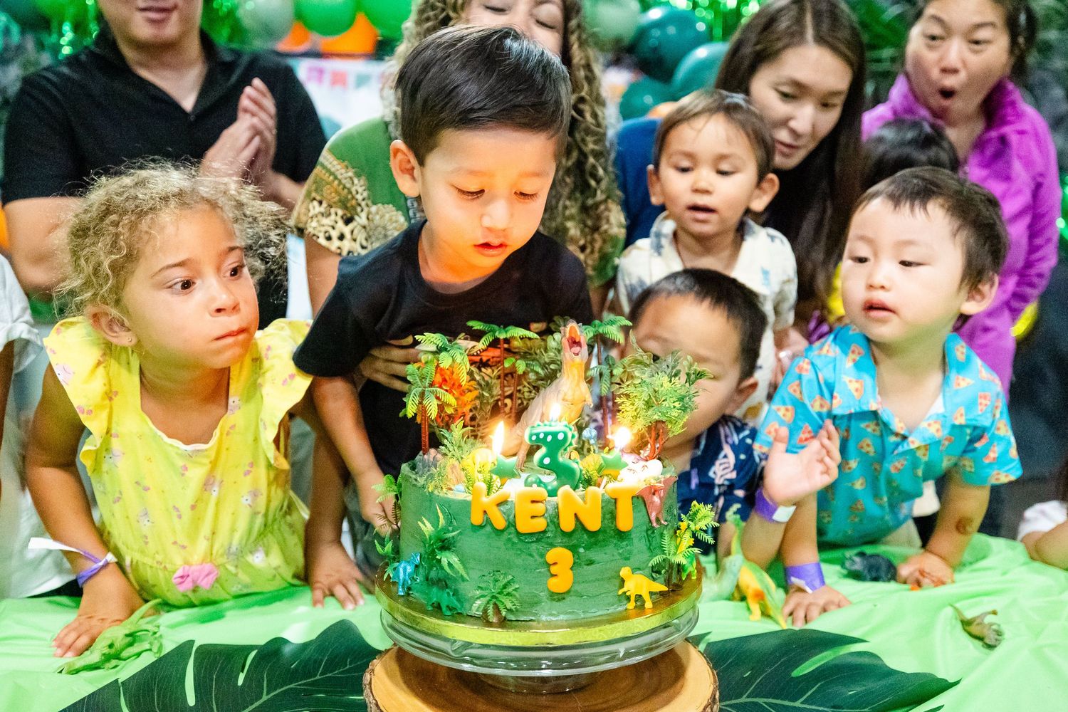 Children blowing out candles on a jungle-themed birthday cake that reads Kent 3.