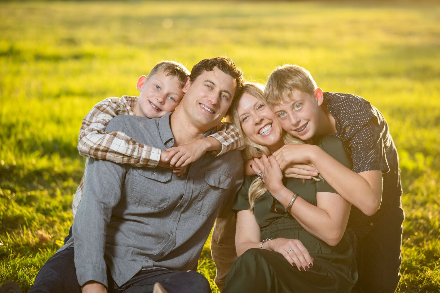 Joyful family of four hugging and laughing together in a sunny green field.
