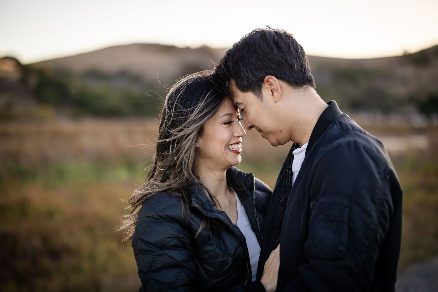 A smiling couple in black leather jackets share a romantic moment outdoors at golden hour.
