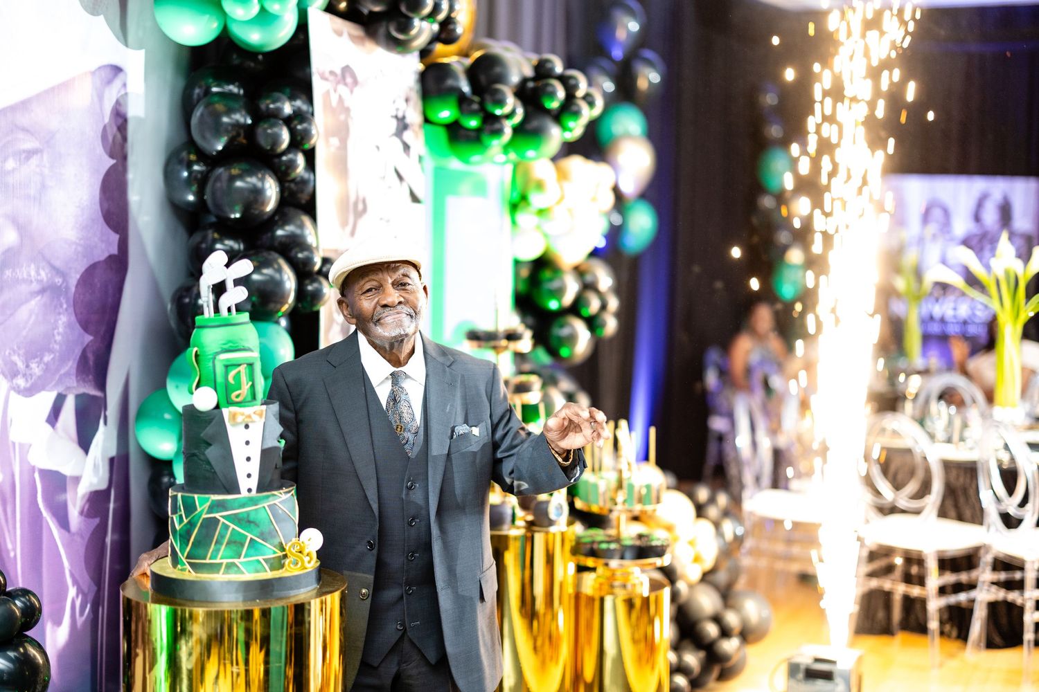Smiling man in a suit celebrating at a green and gold birthday party with balloons.