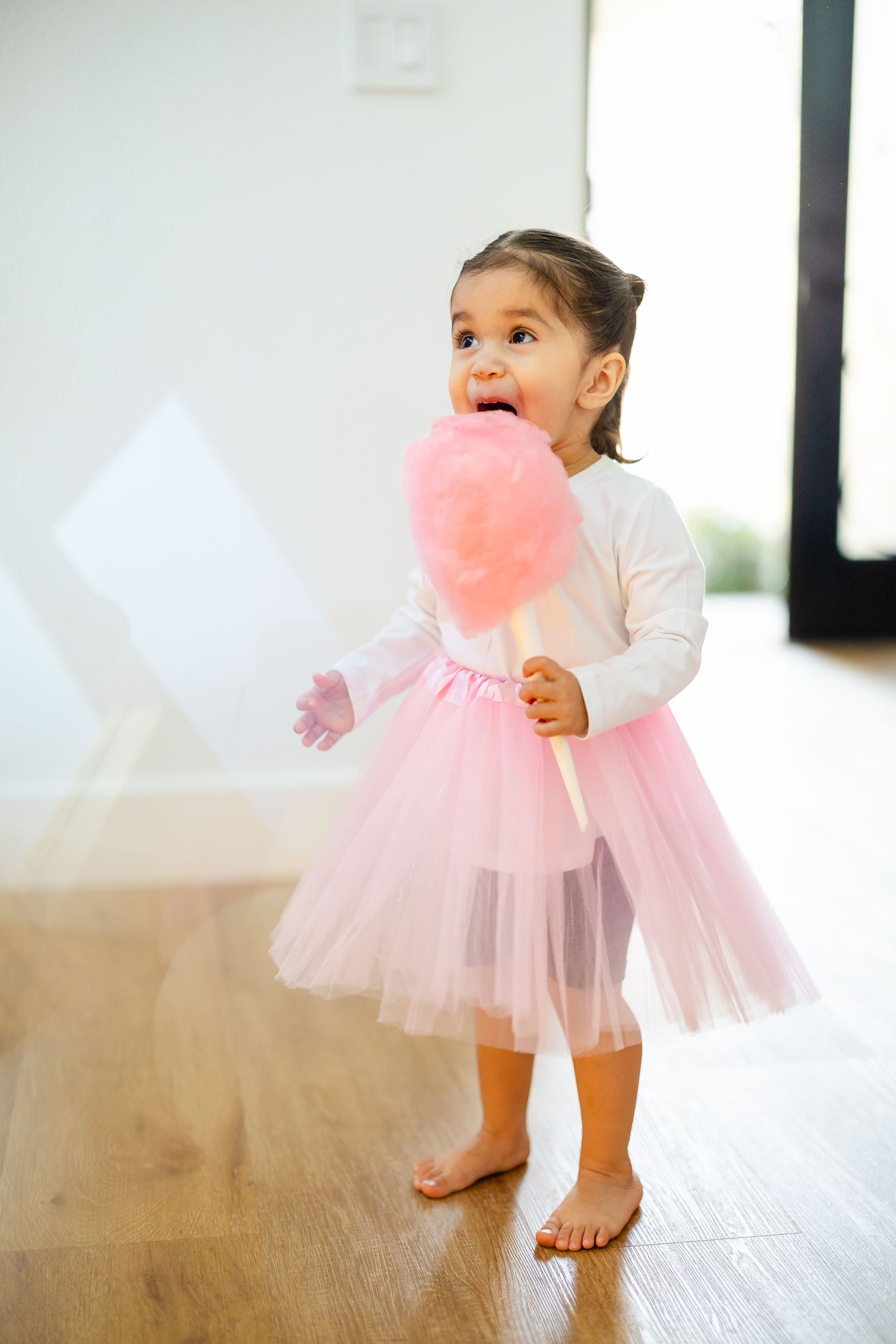 Adorable toddler in pink tutu dress holding a large pink cotton candy stick.