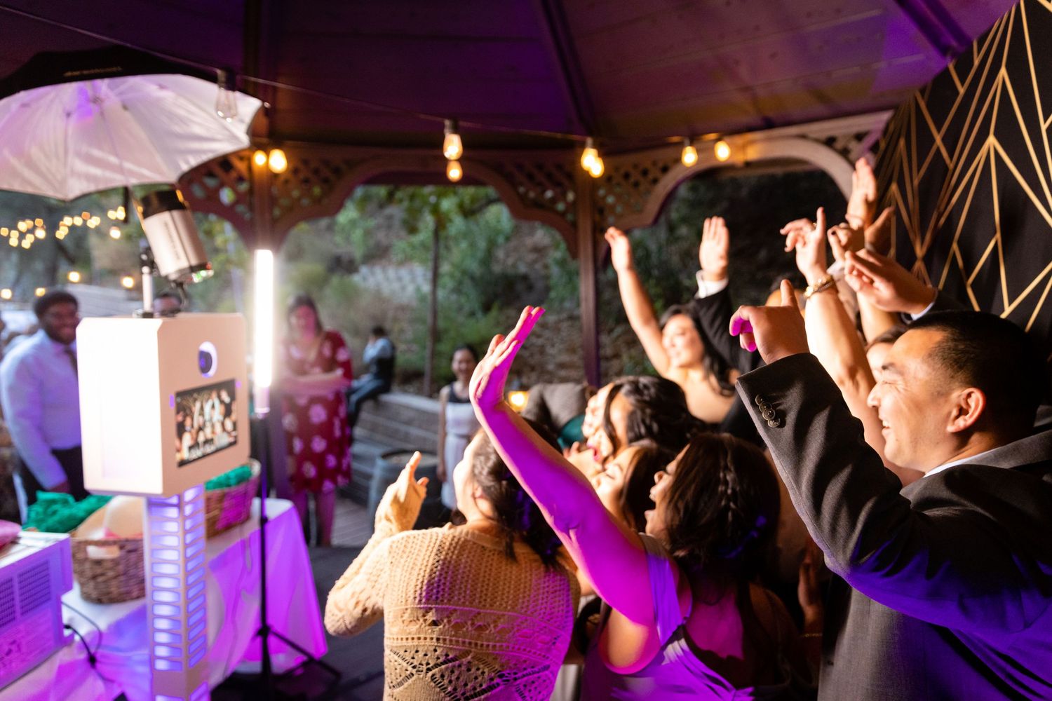 Excited wedding guests dancing and raising hands at an outdoor evening reception.