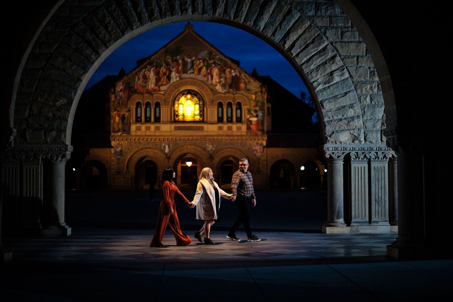 Family walking through an illuminated Stanford University archway at night.
