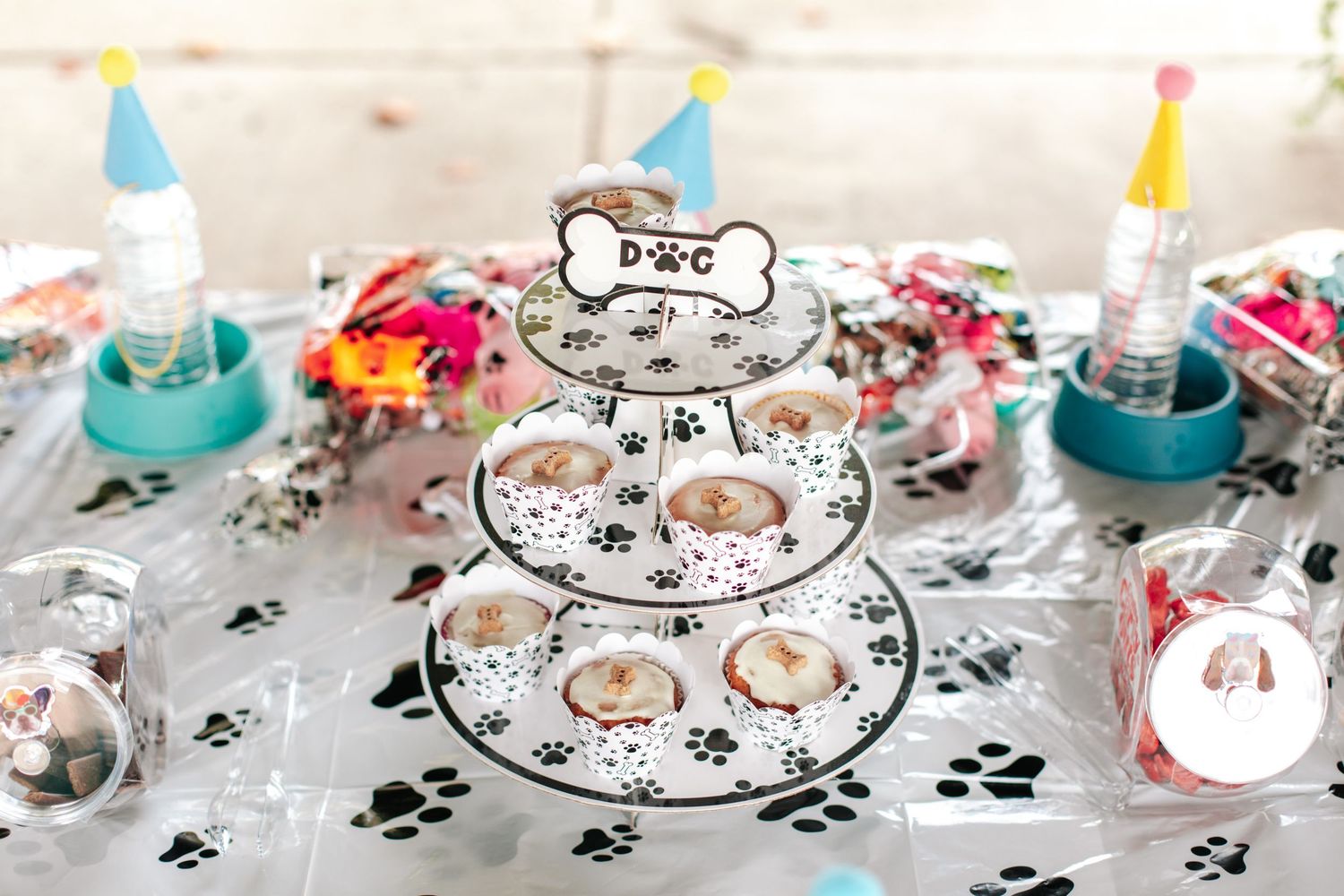 Dog-themed party table with paw print tablecloth, tiered cupcake stand, and colorful decorations.