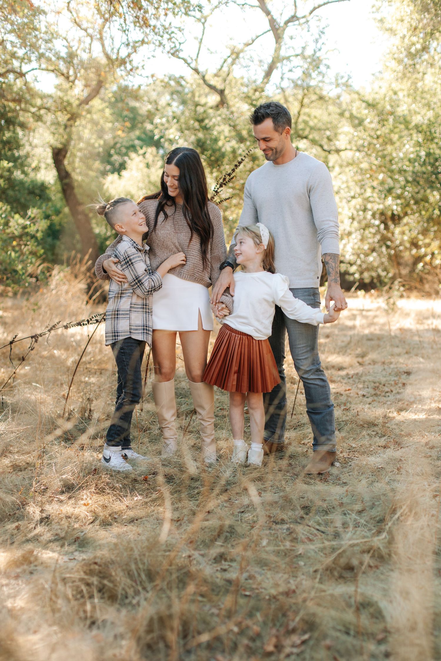 Cheerful family of four laughing and playing together in a sunlit wooded area.